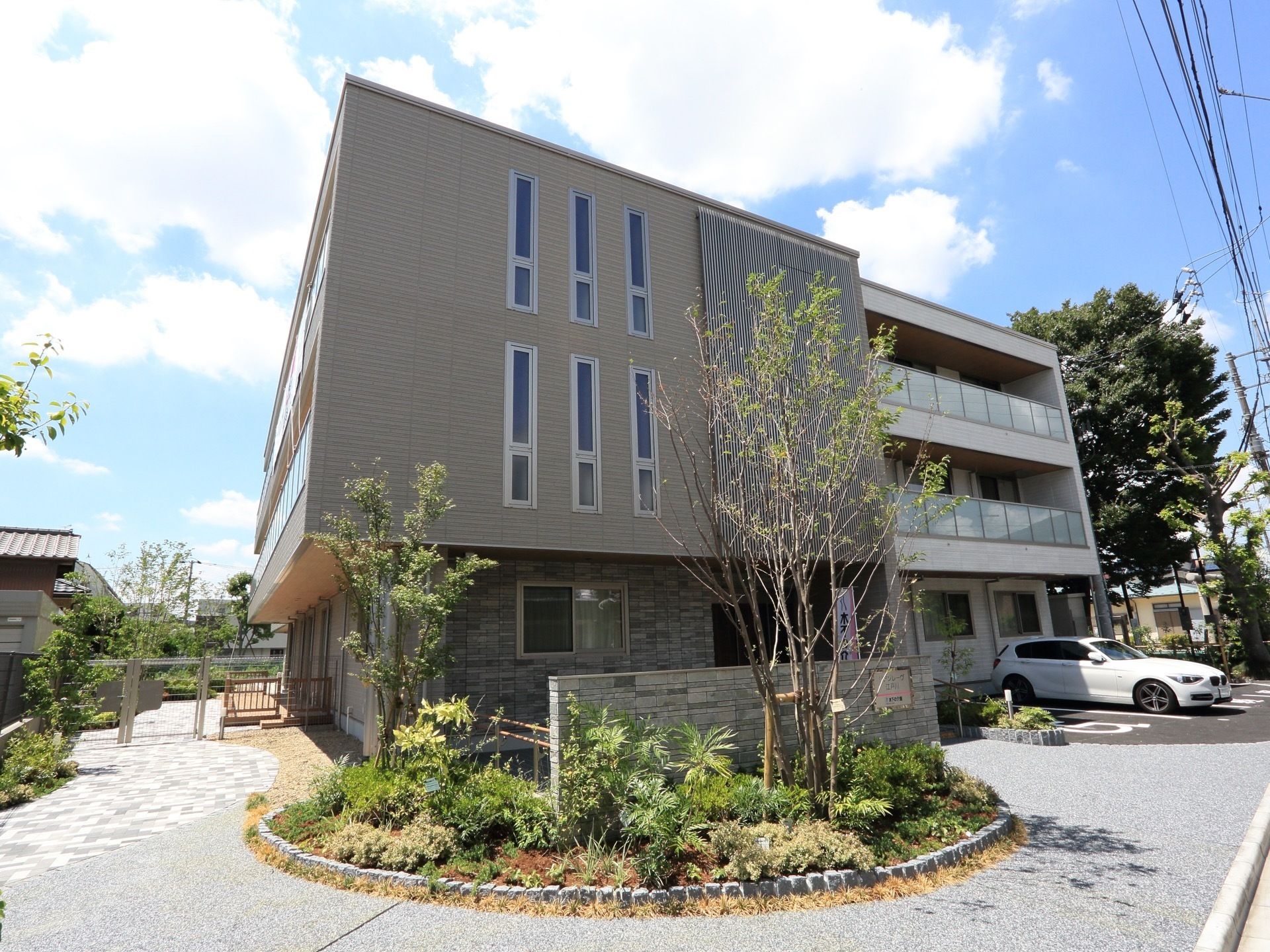 地上３階建ての施設は、ゆったりとした玄関前のスペースに円形の花壇があり、大小の木々が植えられている。奥のスペースは駐車場になっている。