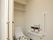 居室のトイレは、壁際に洗浄機能付き便座が設置され便座カバーがついている。床はフラットな木目調のフローリングでお揃いのマットが敷かれいる。