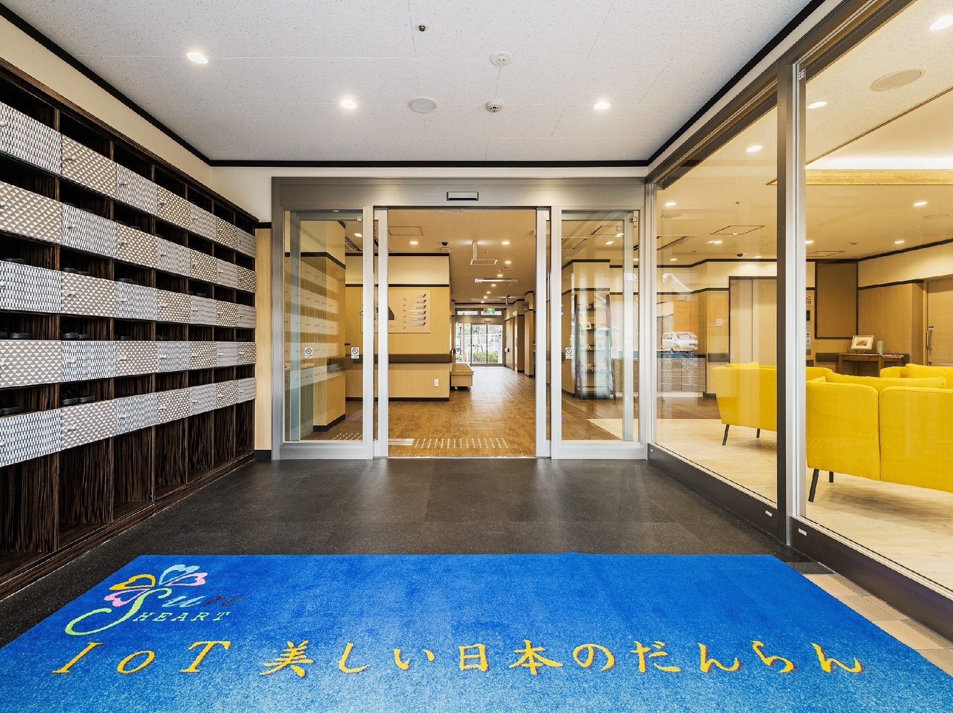 玄関の自動扉、玄関へと続く壁が全面ガラス張りなので屋内の様子が見える。段差がなく幅の広い玄関である。