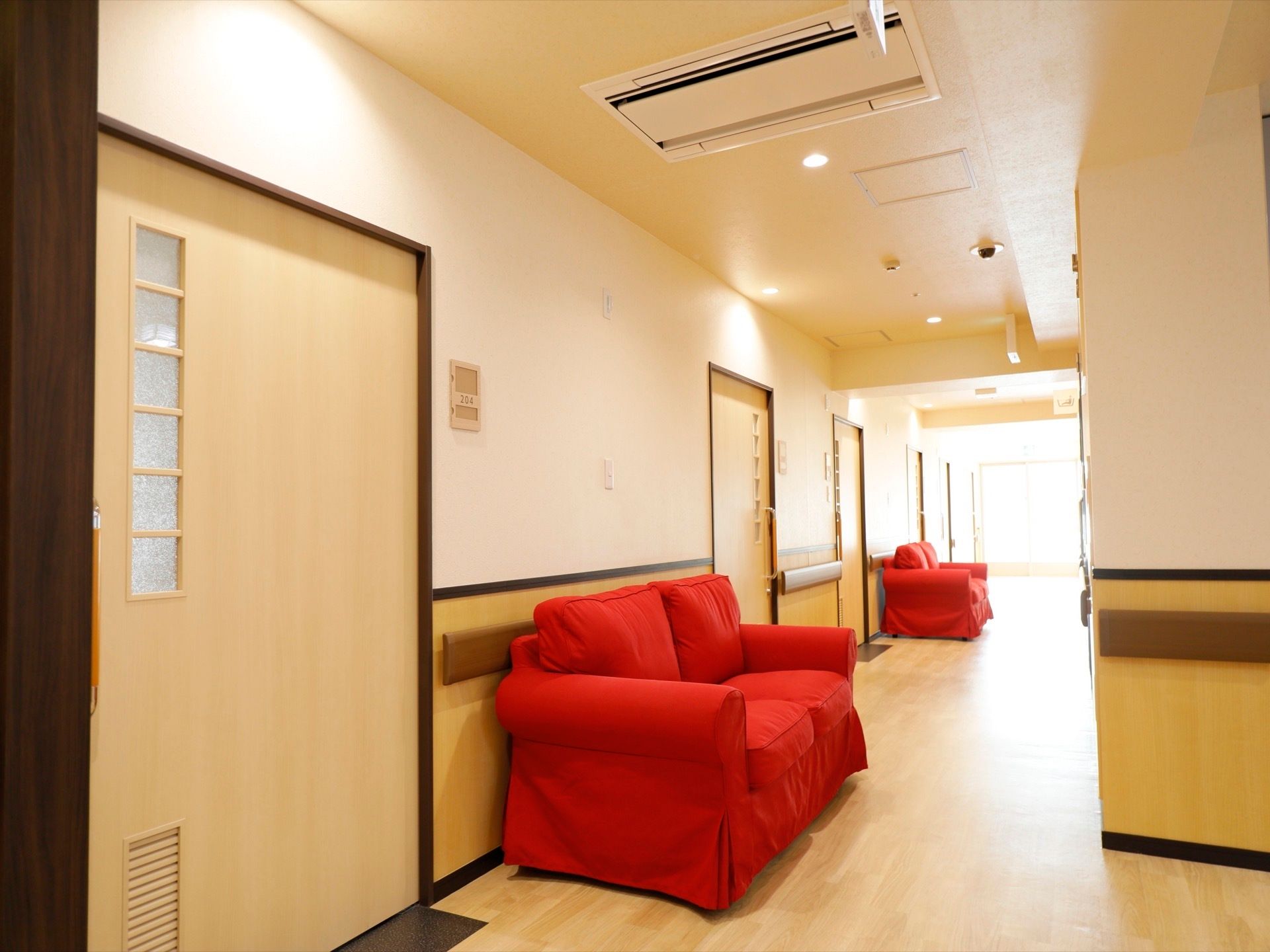 通路には幅の広い手すりが設置されている。居室の扉と扉に挟まれるような形で、２人掛けの赤いソファーが置かれている。