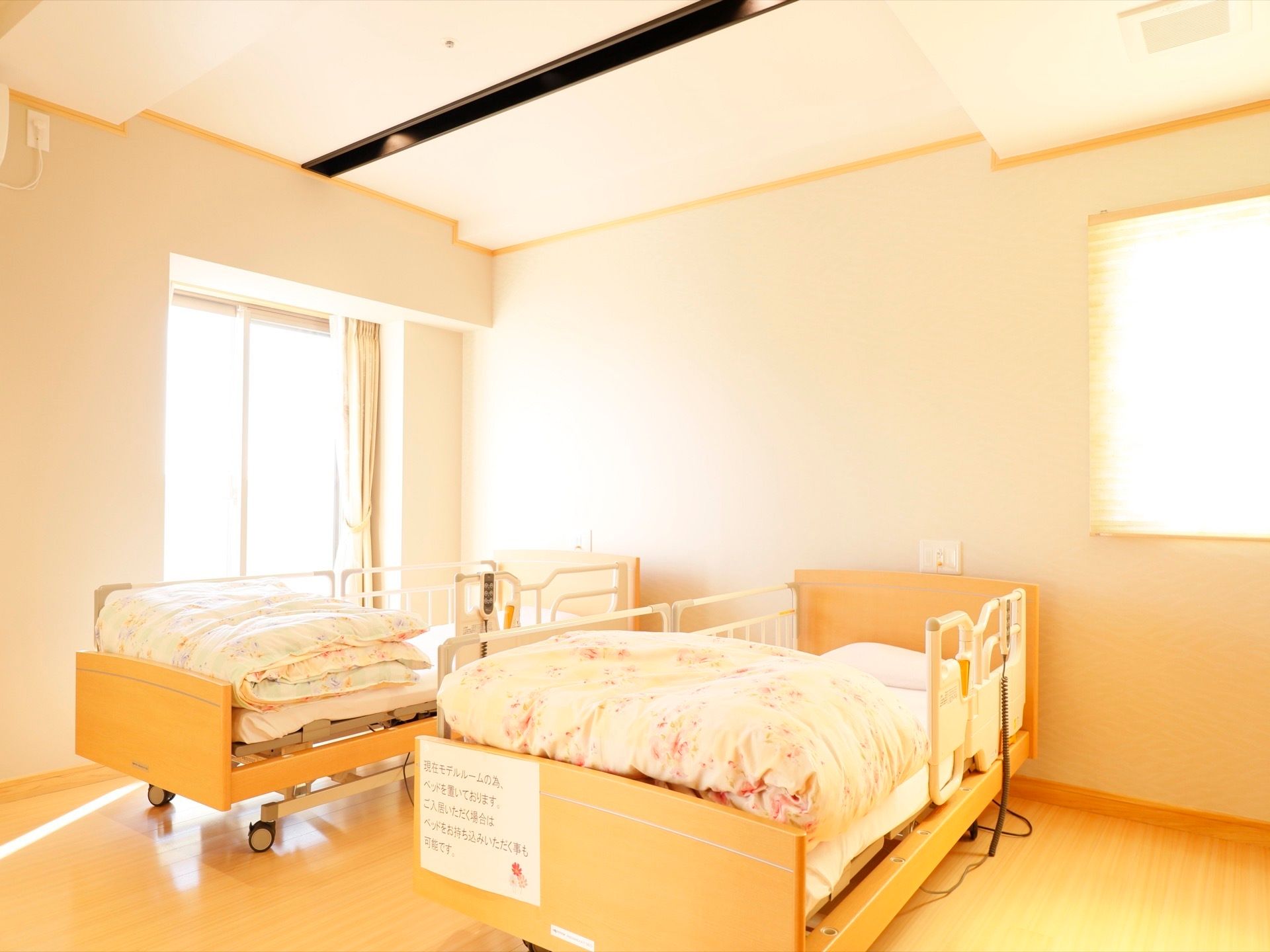 居室の様子である。ゆったりとした室内にベッドが２台置かれている。二面の壁に窓があり、外から明るい光が差し込んでいる。