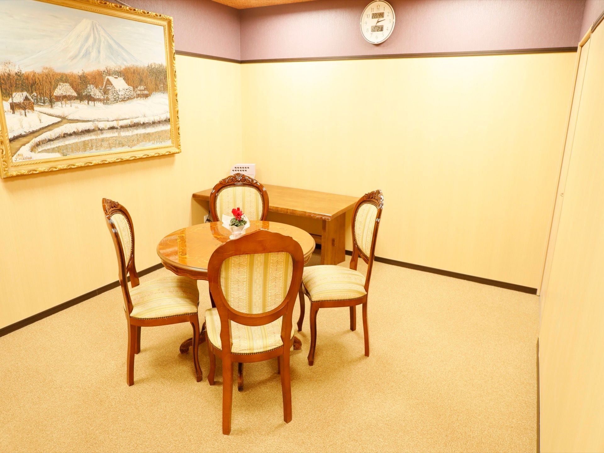シンプルな部屋に、高級感と落ち着きのあるテーブルセットがある。壁には掛け時計と大きな絵画が飾られている。