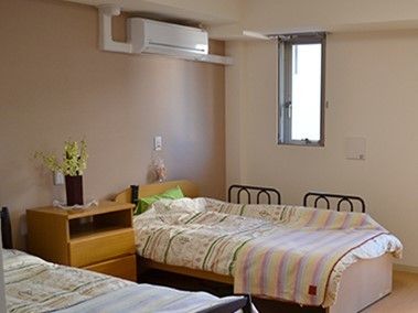 お2人様用の居室は広く、壁際にチェストと介護用ベッドが設置されている。チェストの上には花が飾られている。