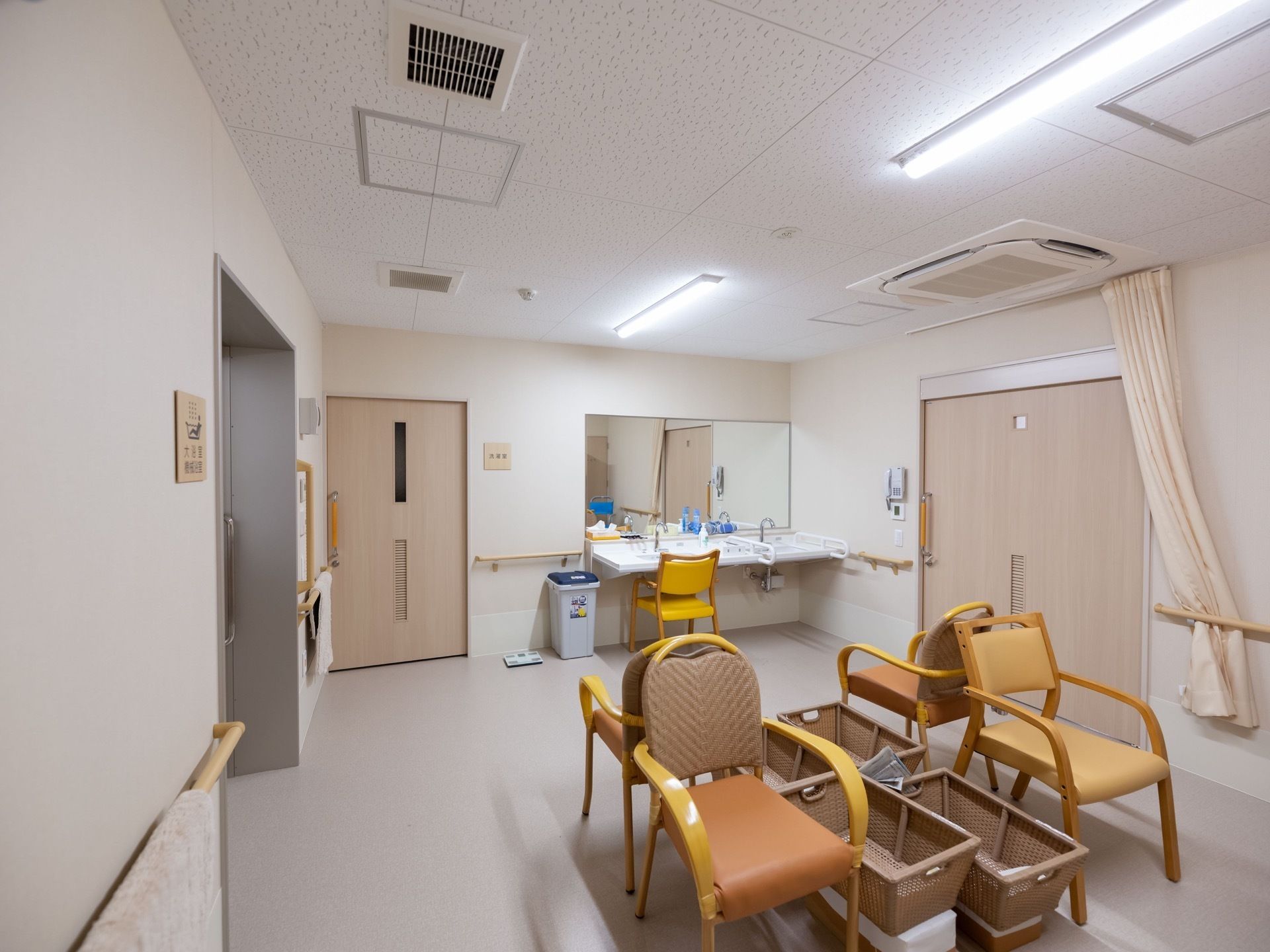 洗面所は広く、洗面台の前には大きな鏡がある。椅子の背もたれをくっつけるように椅子が置かれている。椅子の横にはボックスがある。