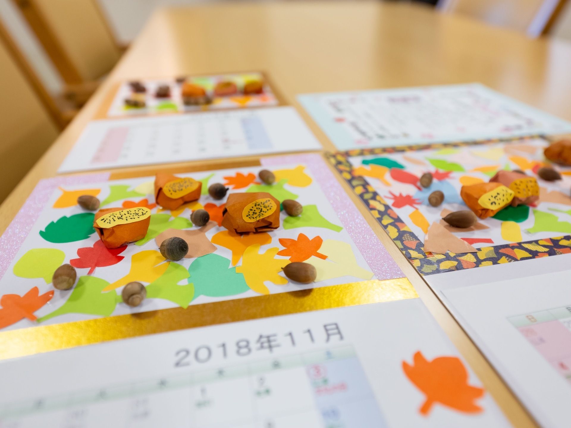 テーブルの上にカレンダーと作品が置かれている。作品は、折り紙で作られたイチョウやもみじ、立体的な栗、本物のドングリがのったものとなっている。