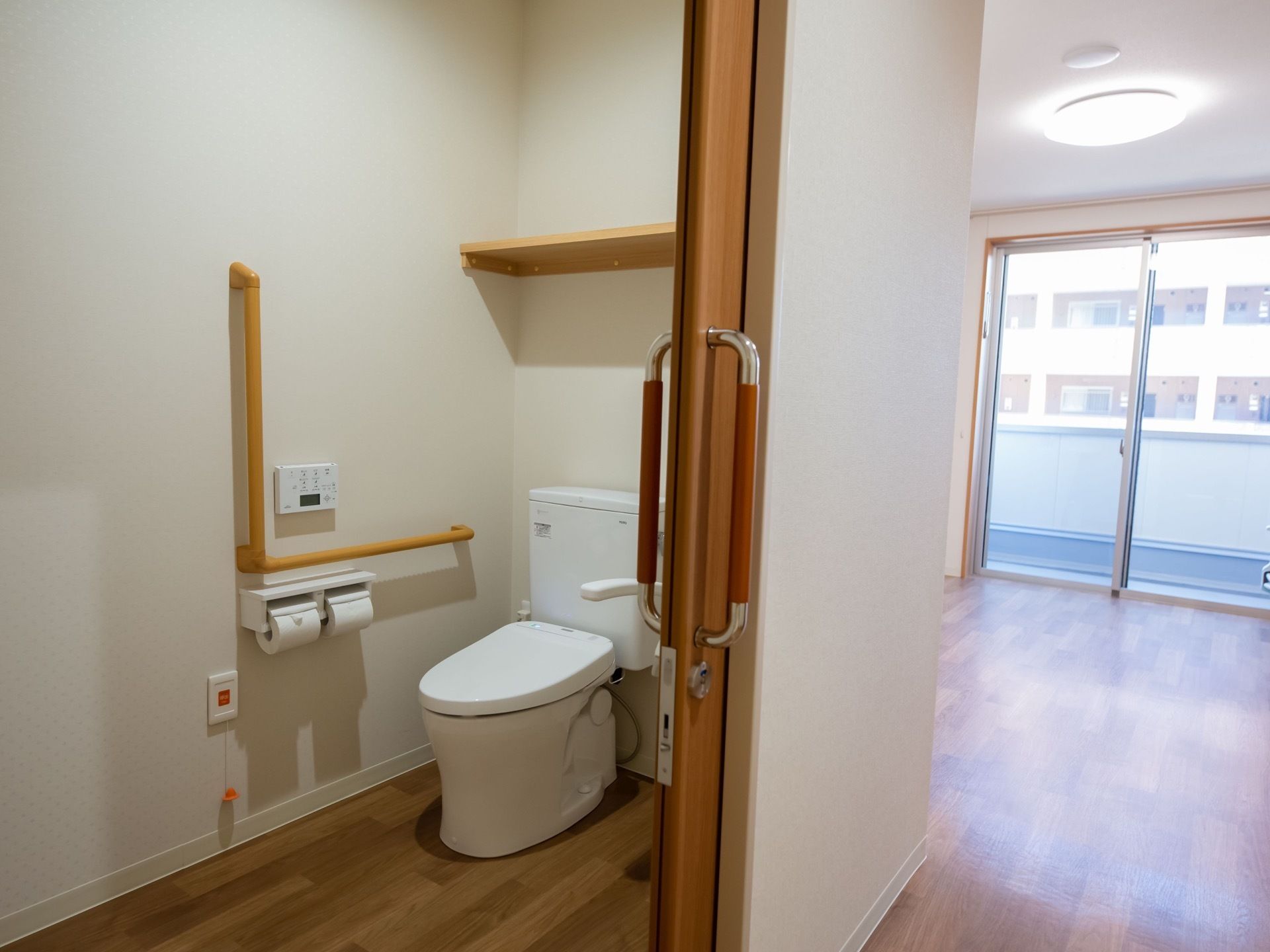 居室は広く、大きな窓がある。トイレには洋式便器が設置されている。壁には手すり、トイレットペーパーフォルダー、呼び出しボタンがある。