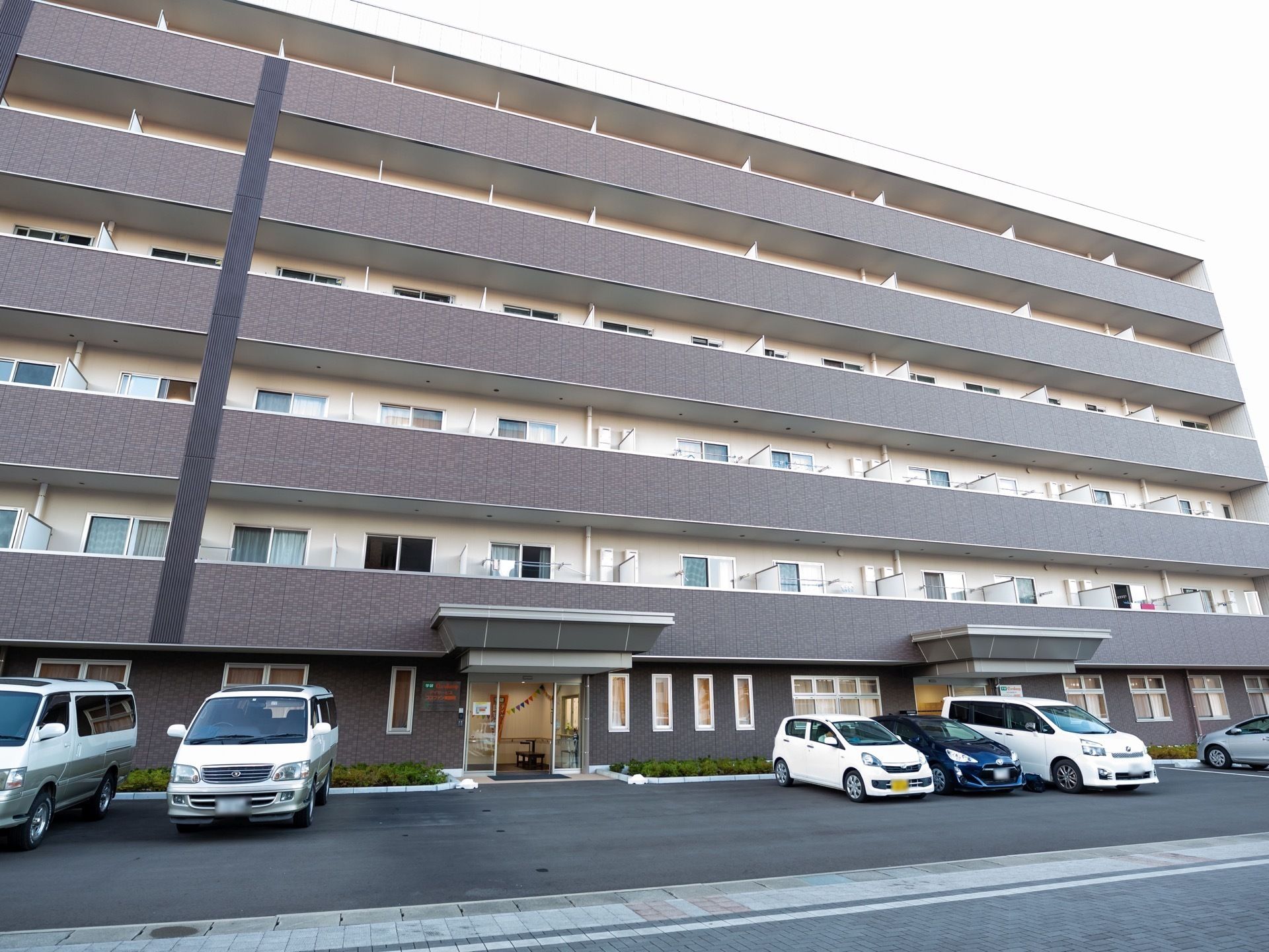 施設前に多くの駐車スペースのある、6階建ての施設の外観