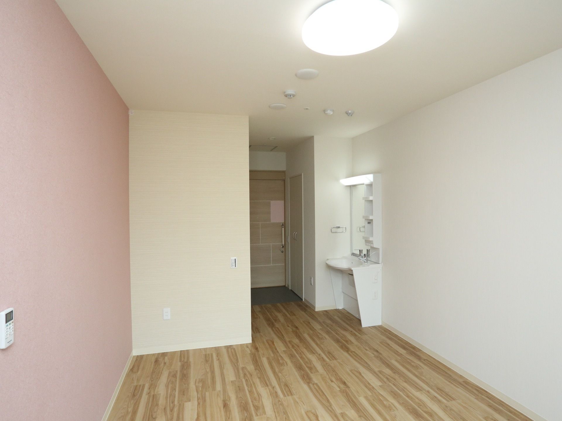 壁片面がピンク色で施された、あたたかみのある個室である。床は木のぬくもりが感じられる木目調のフローリングタイプ。