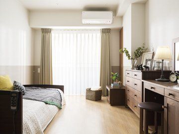 大きな窓がついた明るい居室。テーブルやベッド、タンスなどの家具家電が持ち込まれている。