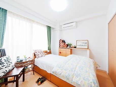 居室にはガラス引き戸が備えられ、壁は白色基調である。床はフローリングになっており、ベッド、椅子、収納家具が設置されている。