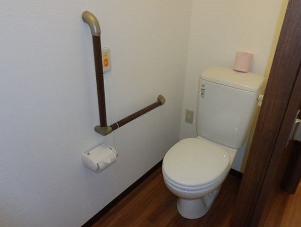 便器はきれいに磨かれているほか、隣の壁には手すりが備え付けられている。手すりのすぐ近くに、施設のスタッフ呼び出し用のボタンも設置されている。