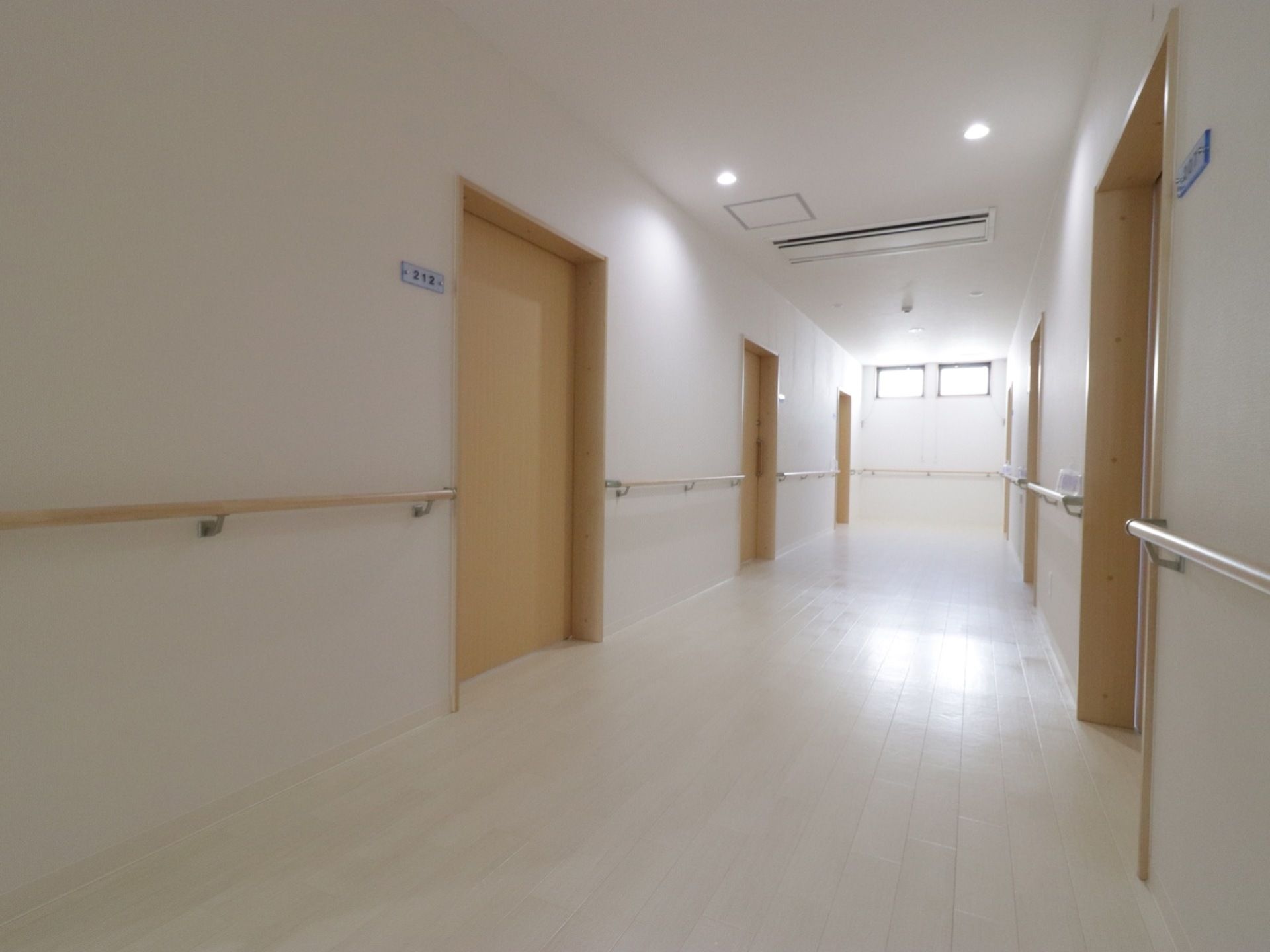 横幅があり広々としている。廊下の突き当りには明り取りの窓がある。天井にはエアコン、壁には手すりを設置している。