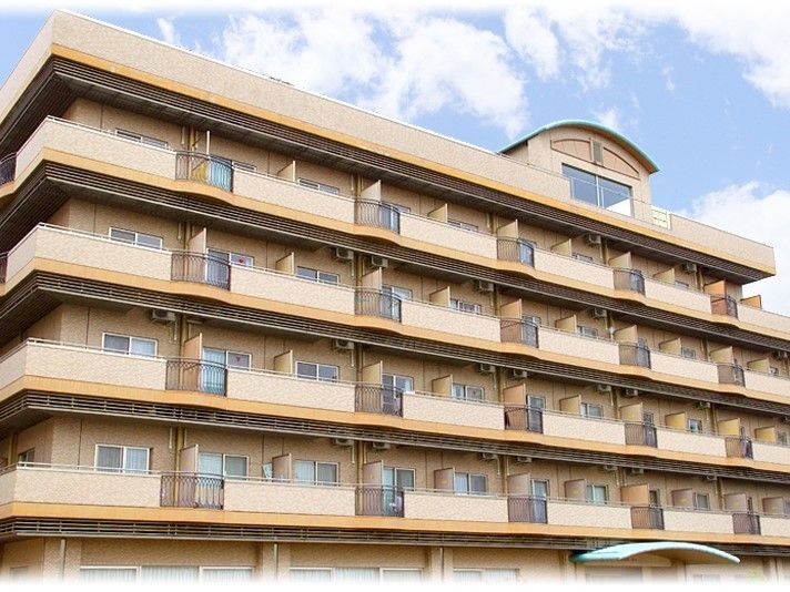 ベージュ色の大きな建物は６階建てになっており、２階から上はすべてベランダがある。玄関庇と６階の屋根一部分が、緑色になっている。