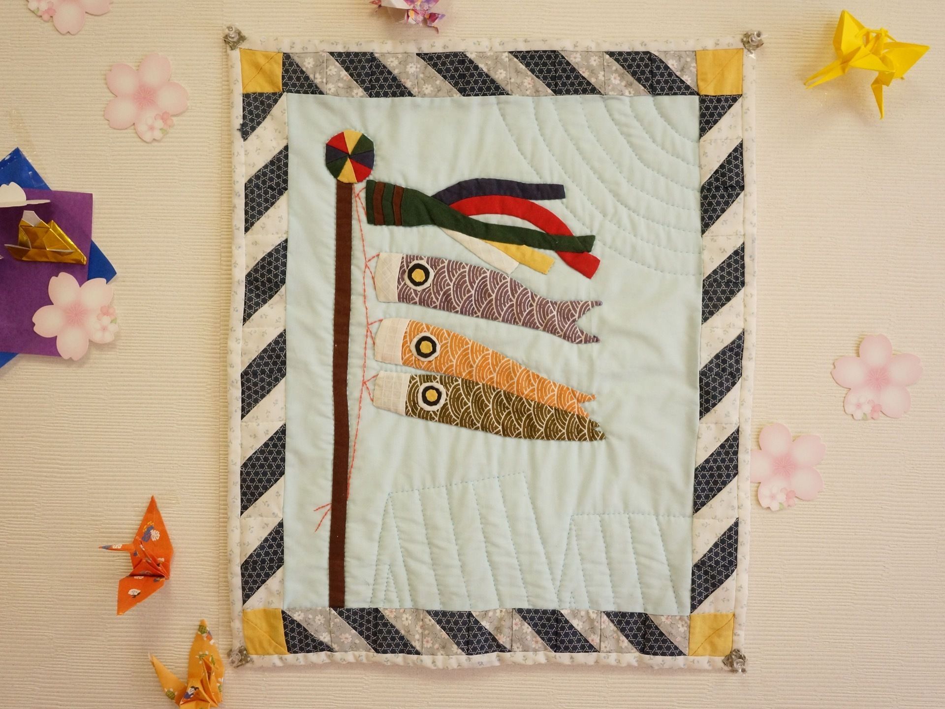こいのぼりの絵が刺繍された、手作りの作品が壁に飾られている。まわりに折り鶴や桜の花びらもデコレーションされている。