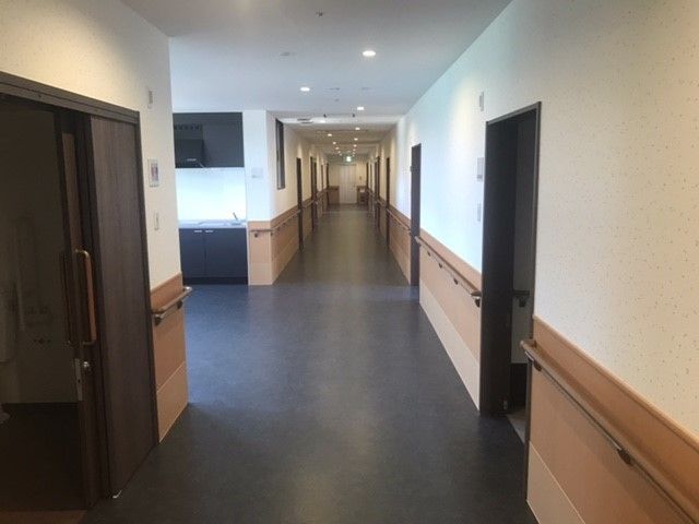 広めの焦げ茶色の床の廊下で、手前左に分かれ道がある。廊下の両側にある各居室のドアは引き戸になっている。