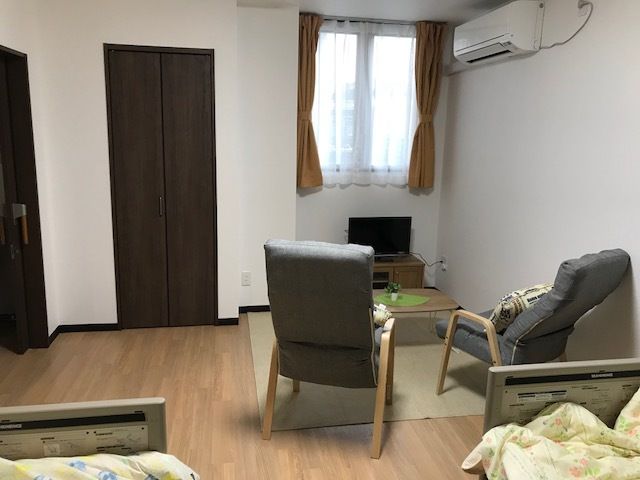 右手前に布張りのリラックスチェアが２脚置かれている。その向こうにローテーブルがあり、奥の一段へこんだ所に小さなテレビが設置されている。