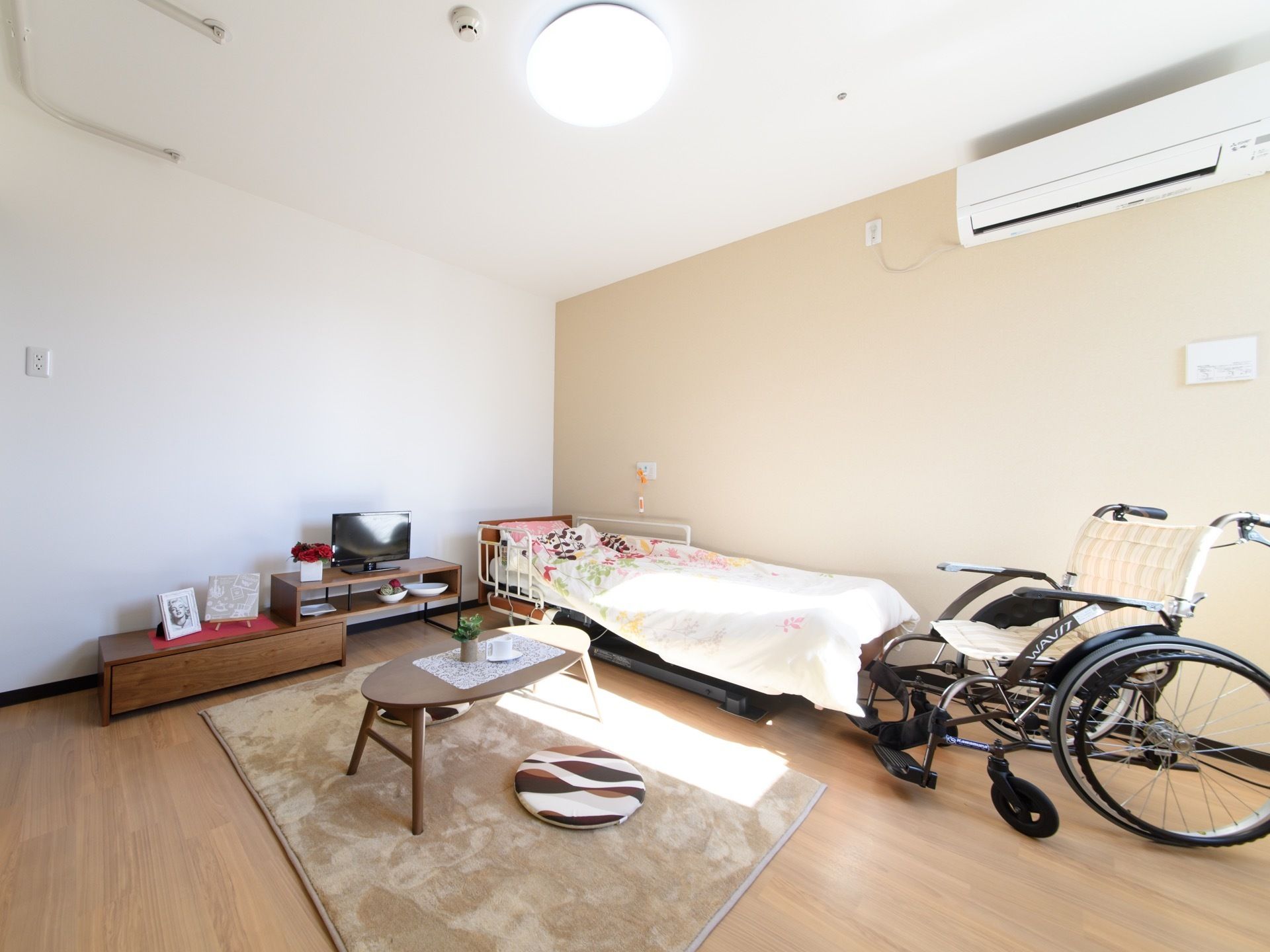 広い居室に、介護用ベット、テーブル、テレビがある。窓からは陽が差し込んでいる。広いスペースで車椅子でも行動し易い。
