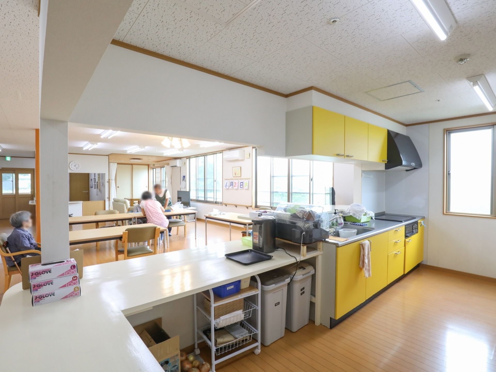 フローリング敷きの広々とした部屋に、Ｌ字型のカウンターキッチンが設置されている。カウンターの裏側には、ごみ箱や棚が置かれている。