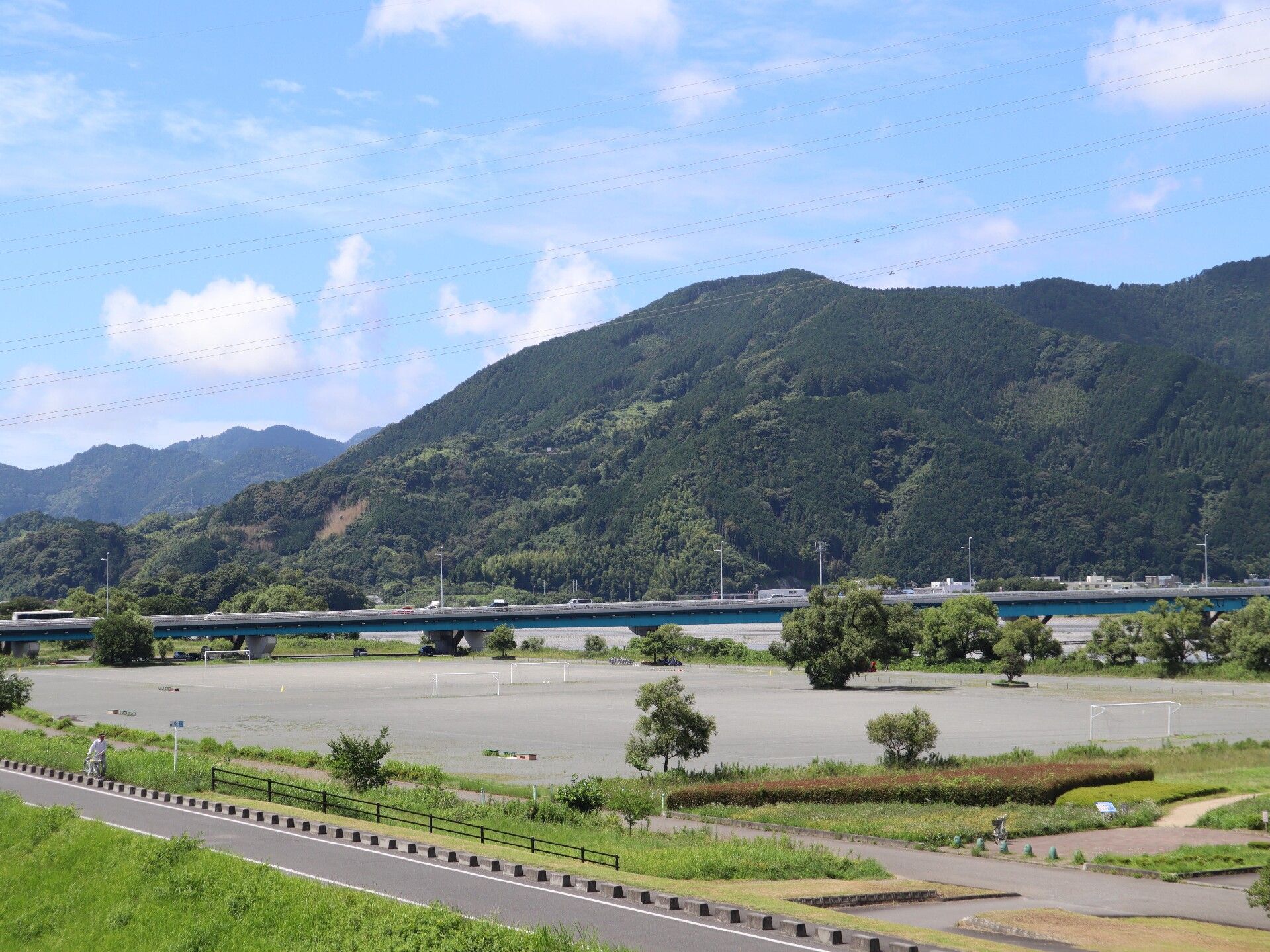 目の前に小高い山が臨める、緑に囲まれた自然豊かな川沿いの道