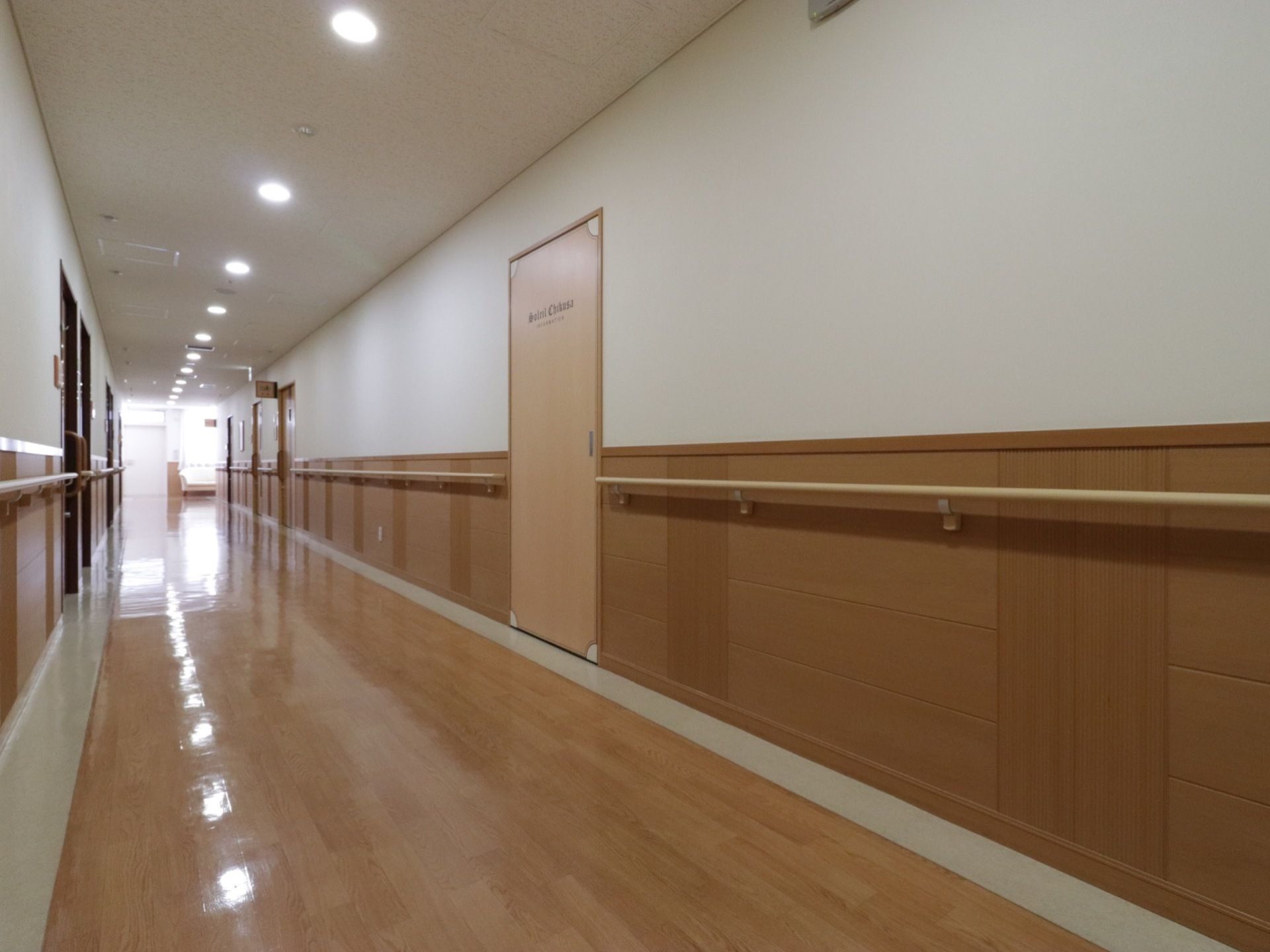 床と壁の下半分と扉が木目調になっている。手すりも木目調である。壁の上半分と天井は白く、照明も白色である。