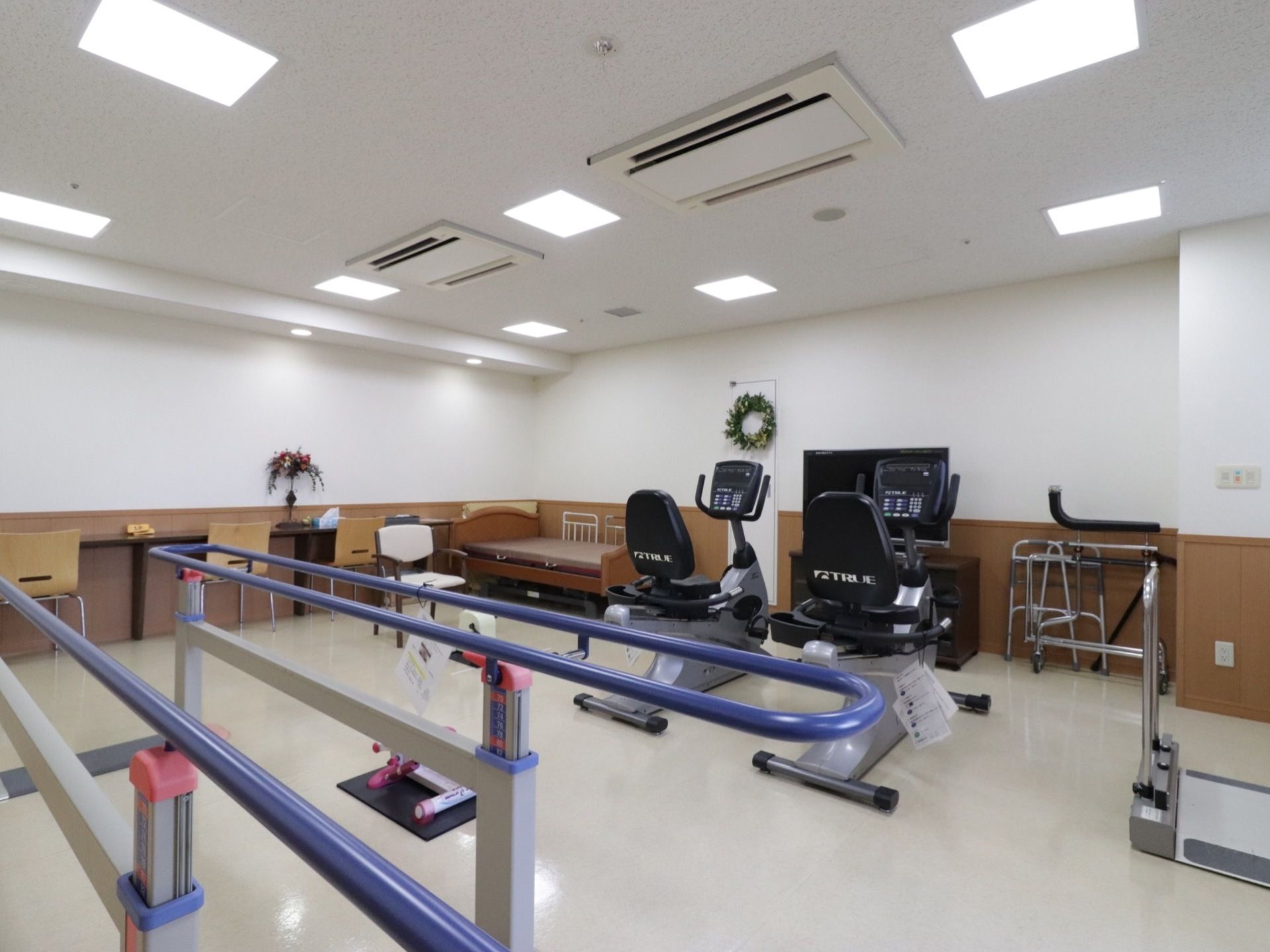 ペダルをこぐタイプの健康器具が２つある。壁にはテーブルと椅子がおいてあり、ベッドで休憩することもできる。