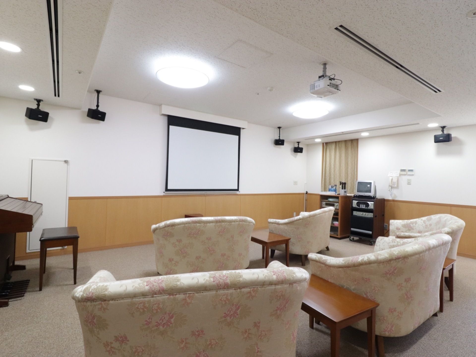 壁にプロジェクターが映せるようになっている。一人掛けソファが５つあり、その間には小さめのテーブルが置いてある。