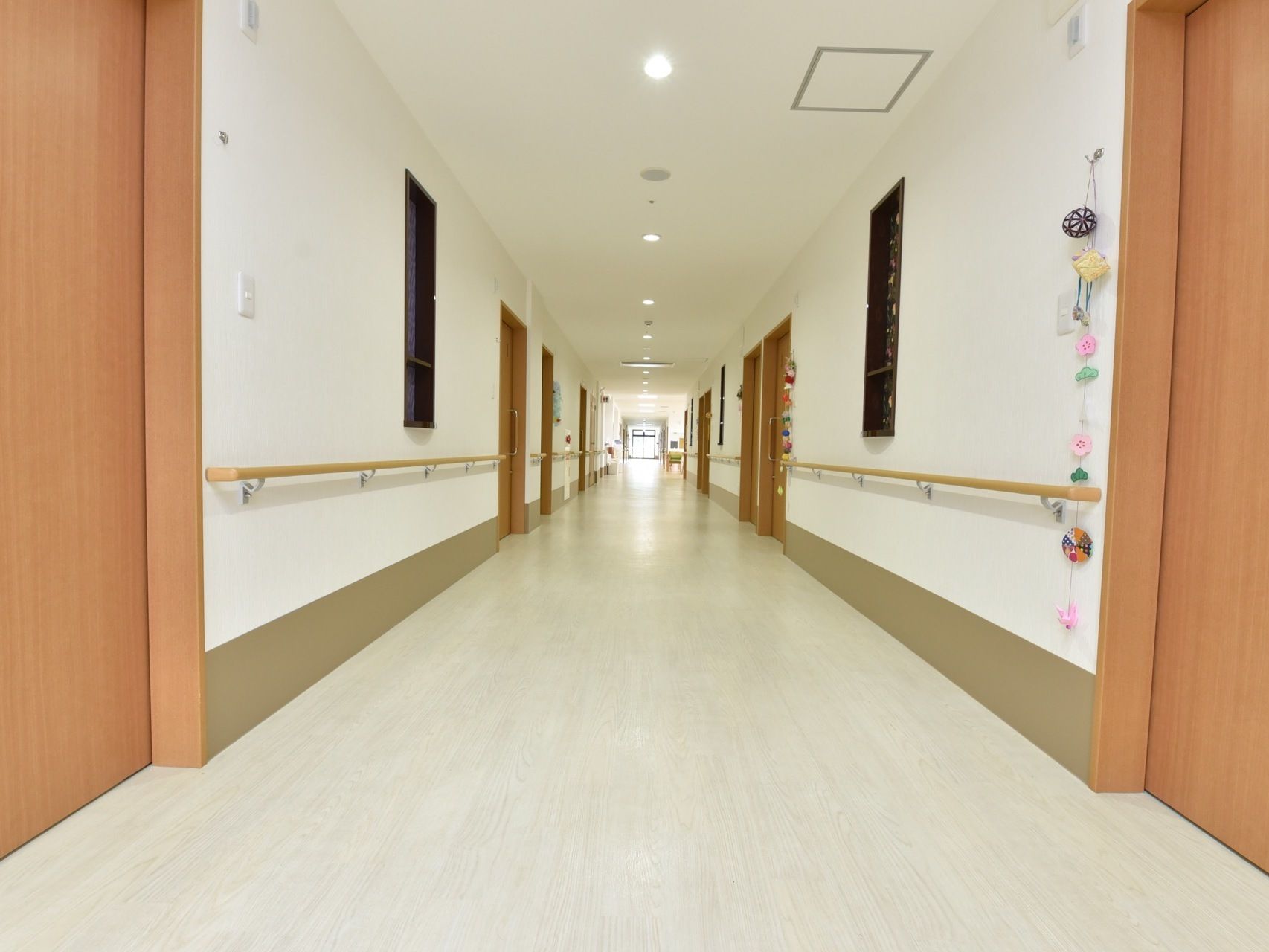 幅の広い廊下になっている。両側には手すりがしっかりと設置されている。突き当りの窓からの日差しや天井の照明で明るい。