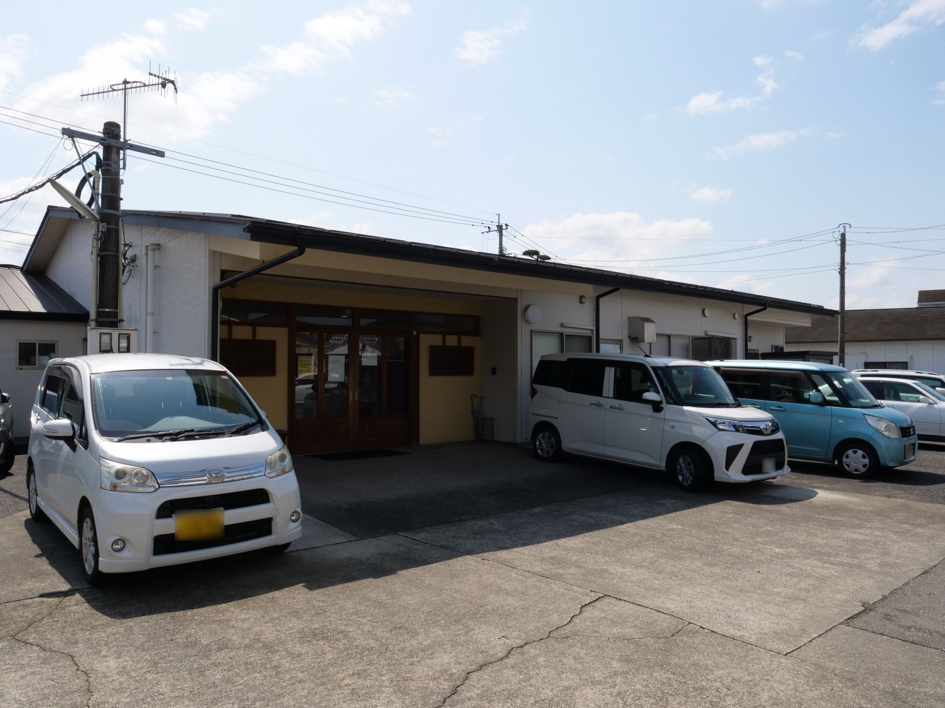 車椅子に乗って手を振る高齢女性と後ろで介助をする女性ヘルパー