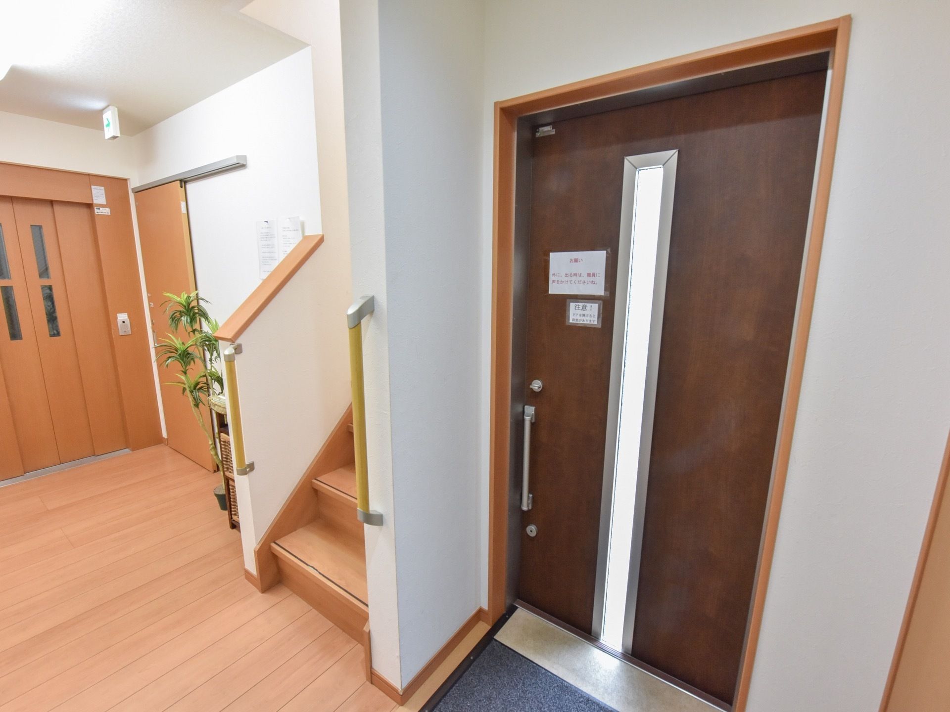 入口はバリアフリーになっている。玄関横に階段があり、その奥にはエレベーターが設置されている。階段横には観葉植物が置かれている。