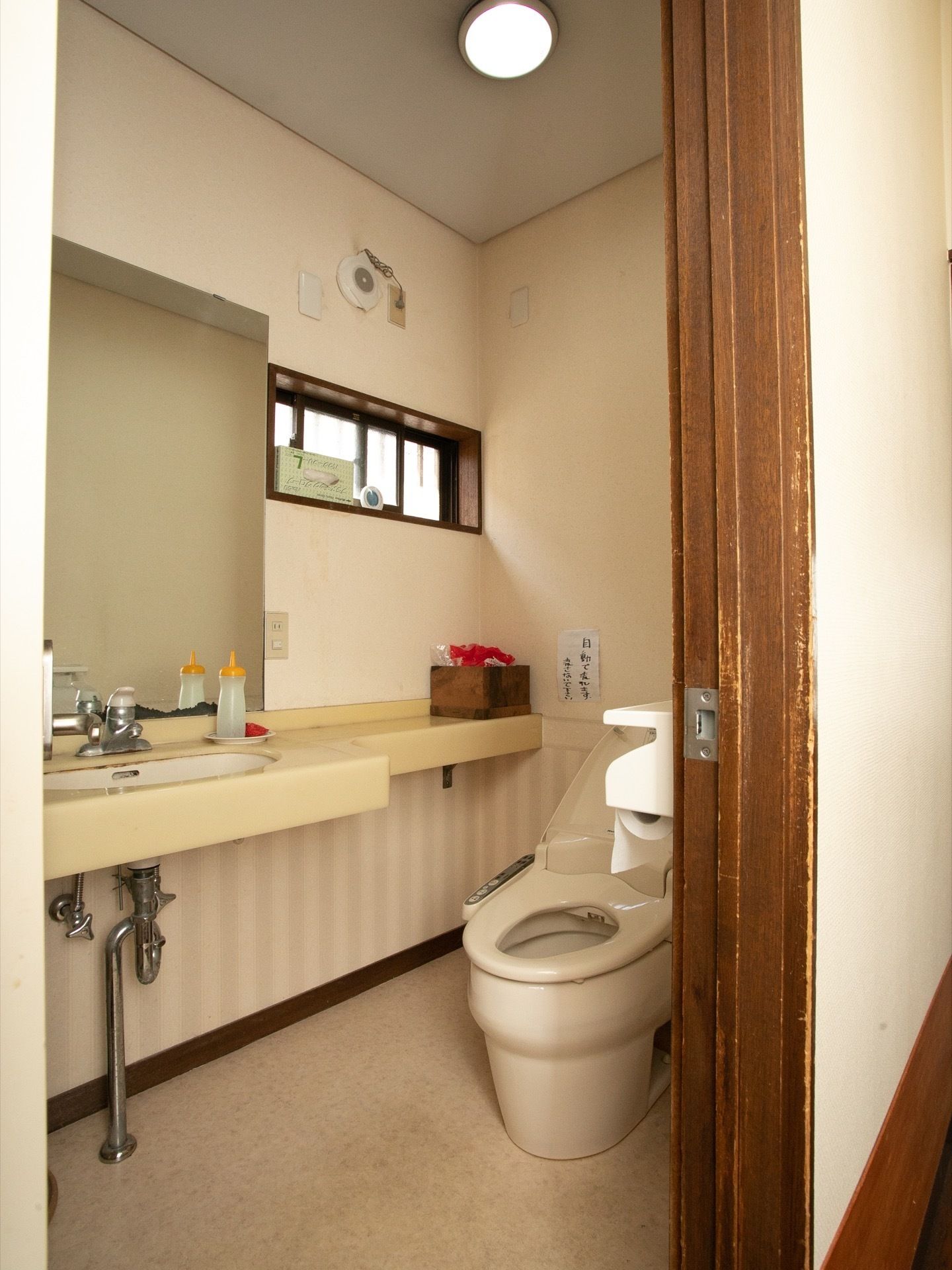 ホーム内にあるトイレ。扉は開いていて、クリーム色の鏡付きの洗面台と、白い洋式トイレの便器が設置されている。