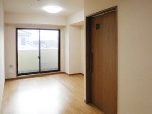 ワンルームのベランダ付きの個室。居室の入口近くの通路には、小窓のついたスライド式のドアが取り付けられている。