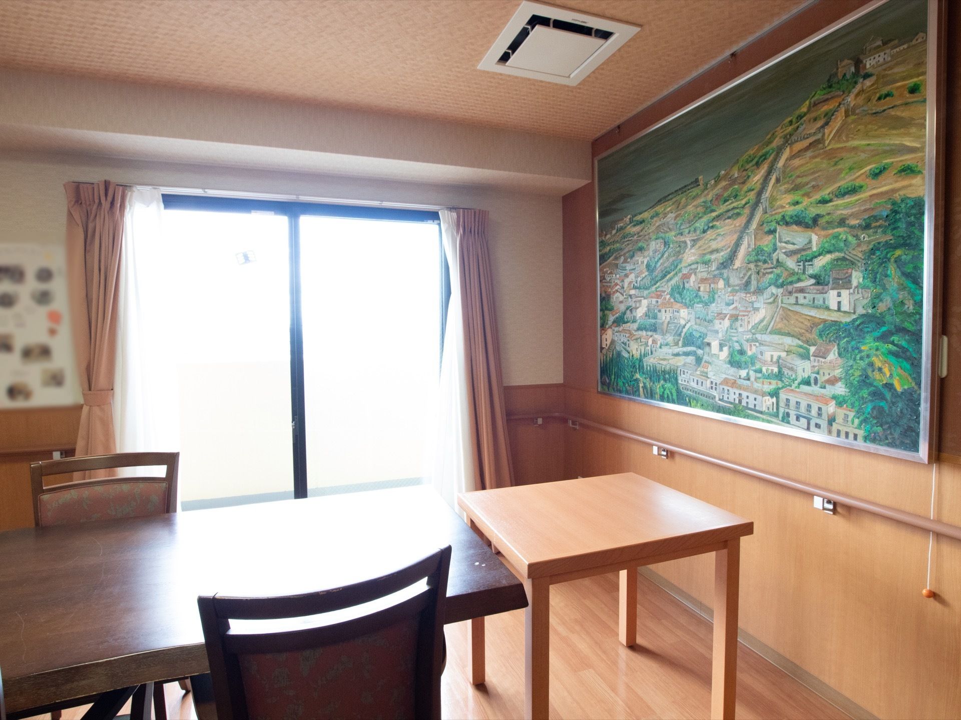 壁に大きな絵画を飾っている。テーブルを置き、椅子をセットしている。横側に大きなガラス戸があり、日の光がお部屋の空間を明るく照らしている。
