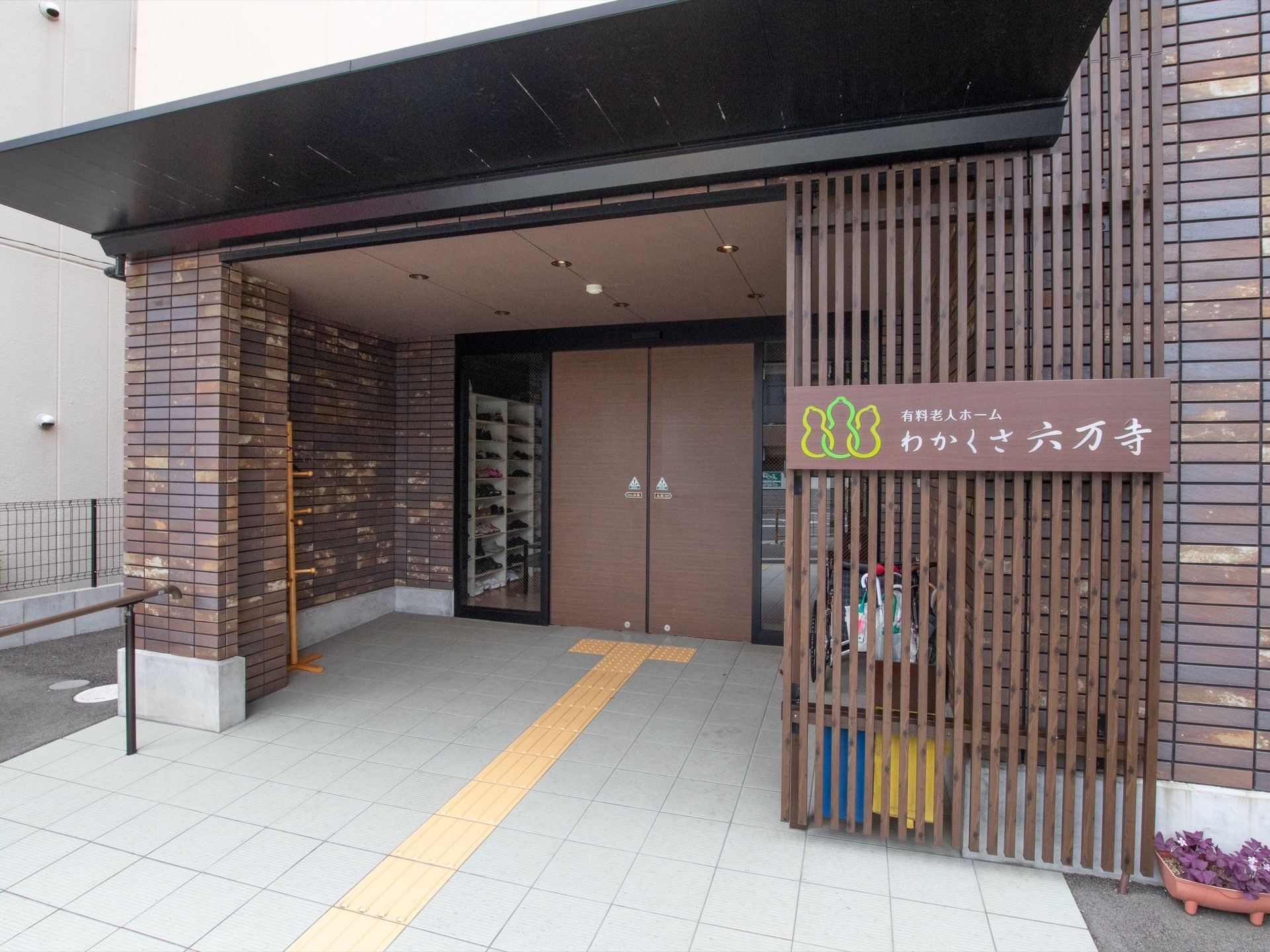 茶色い自動ドアまでの床には、点字ブロックが敷かれている。屋根がついており、入口ドア付近には傘立てがある。