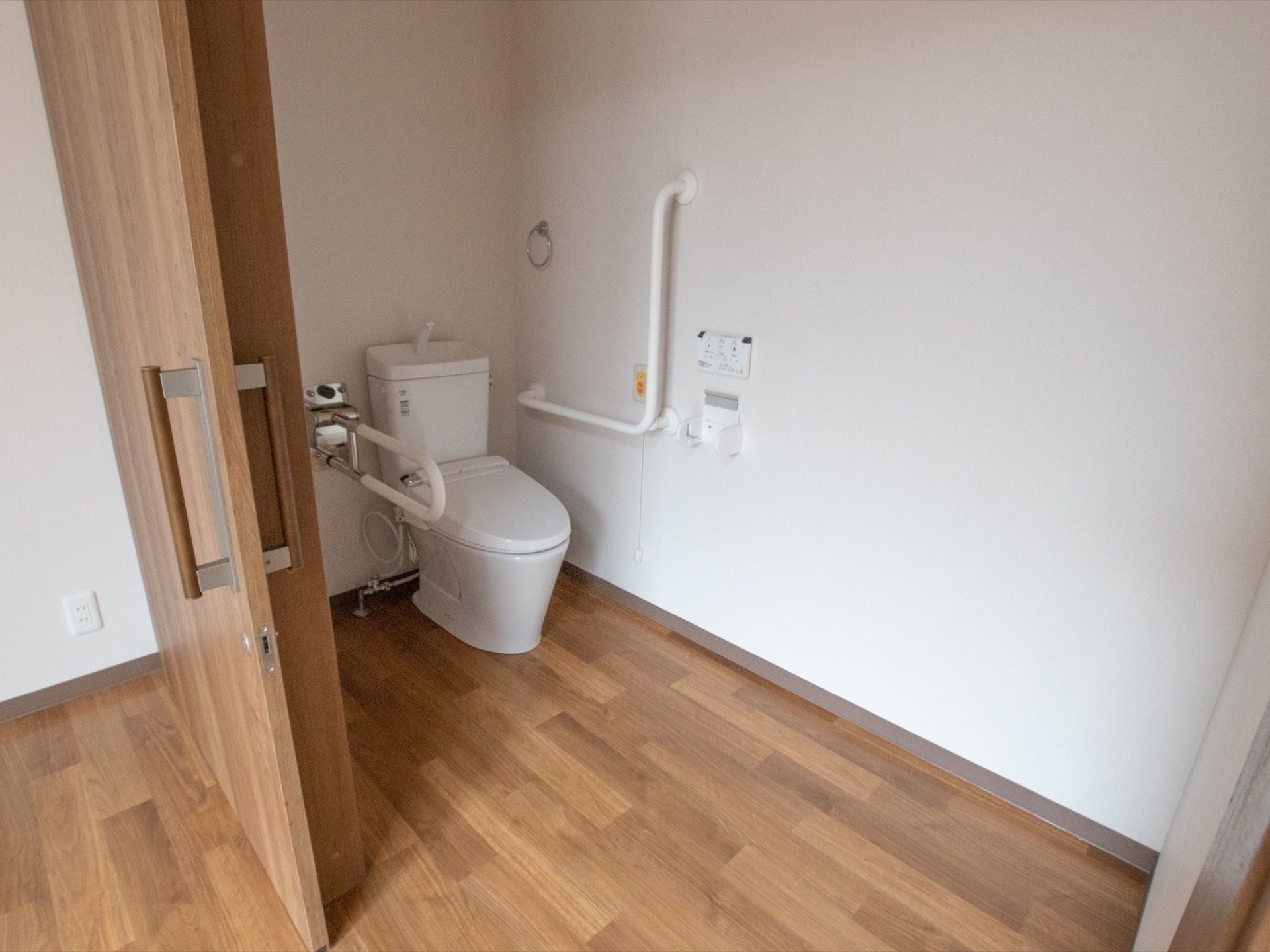 居室内にトイレが備わっている。扉は引き戸で開口が広い。床はフラットで便器の前にスペースを確保している。