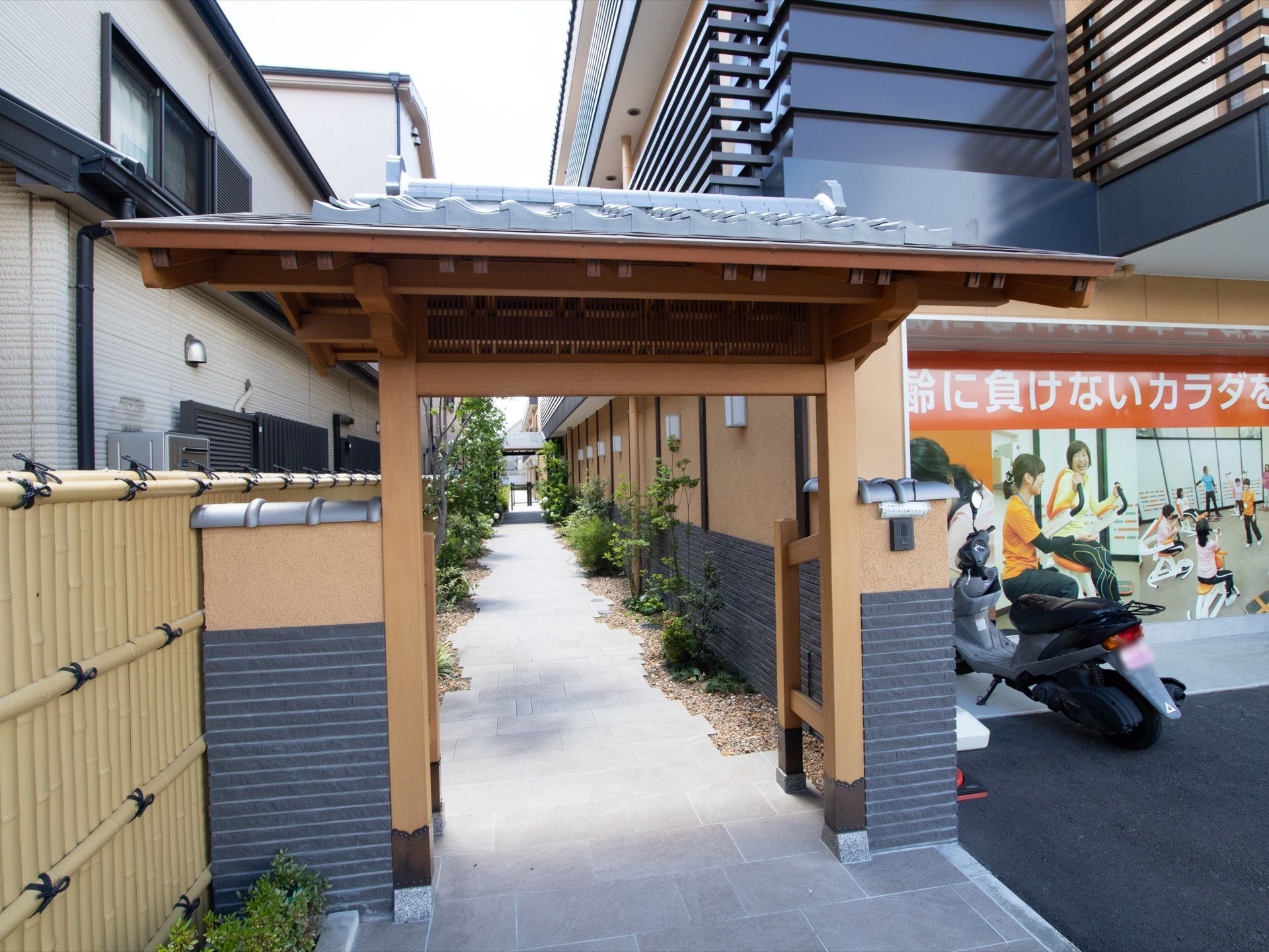 数寄屋門から、玄関に向かうアプローチがまっすぐに伸びている。隣家との境界には竹垣風のフェンスが建てられている。