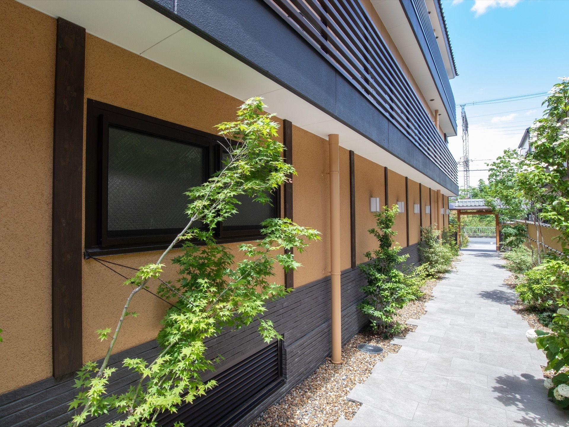 門からまっすぐに長いアプローチが続いている。建物１階の外壁に、通路を照らすための四角いライトが並んでいる。