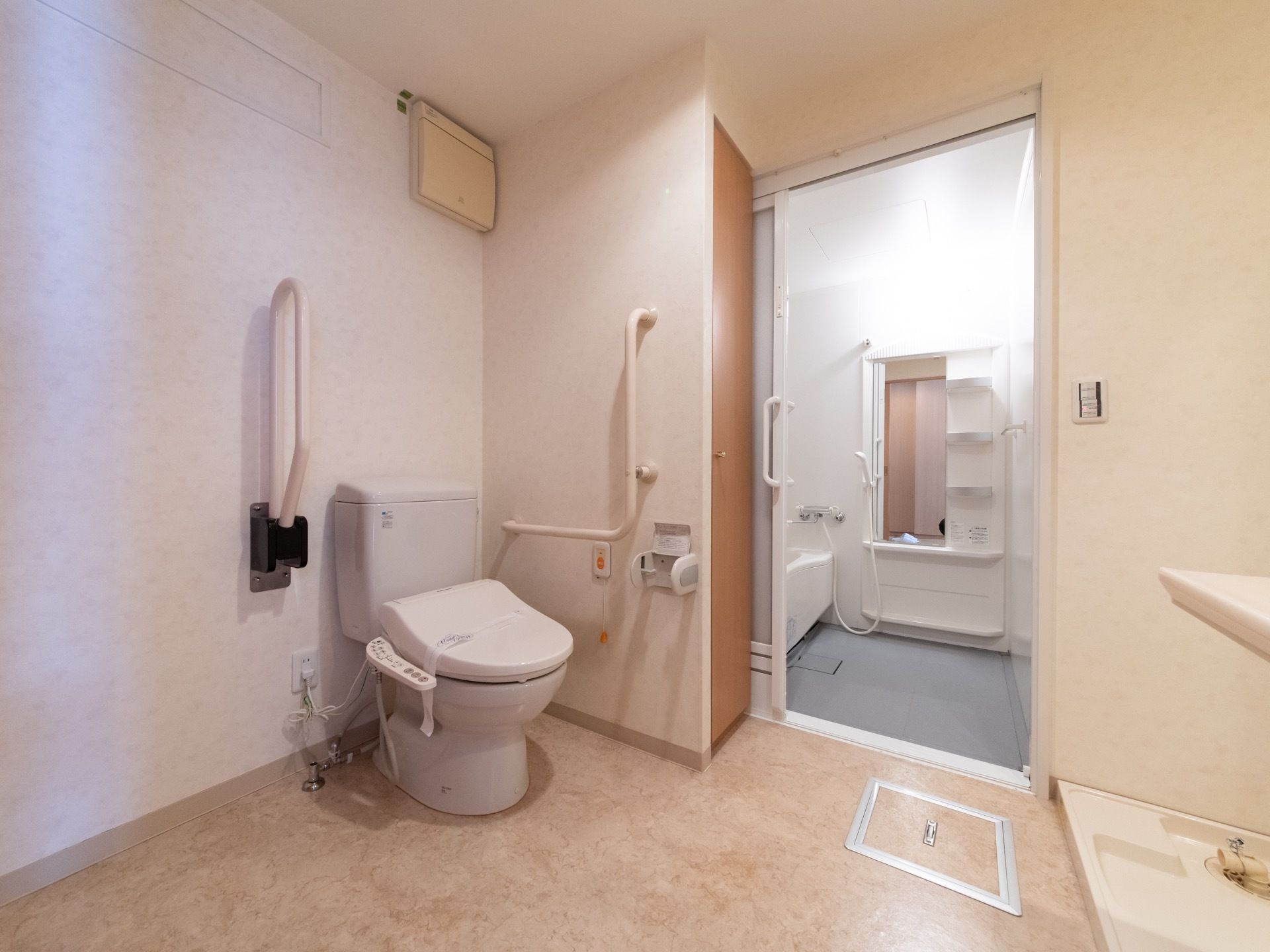 浴室の隣の広々としたスペースにトイレを備えている。横の壁に大きなＬ型の手すりを設置している。反対側の角には、洗濯機置き場を設けている。