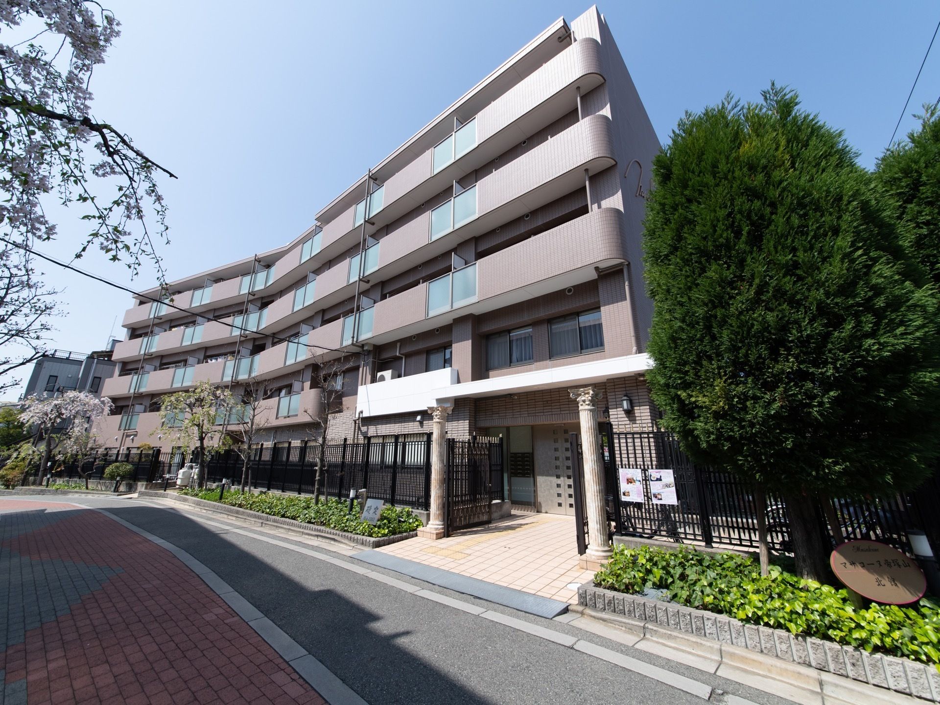施設の建物は、道を挟んで３階建ての棟と５階建ての棟がある。黒の格子の柵があり、さまざまな樹木や植物を植えた花壇が道沿いに連なっている。