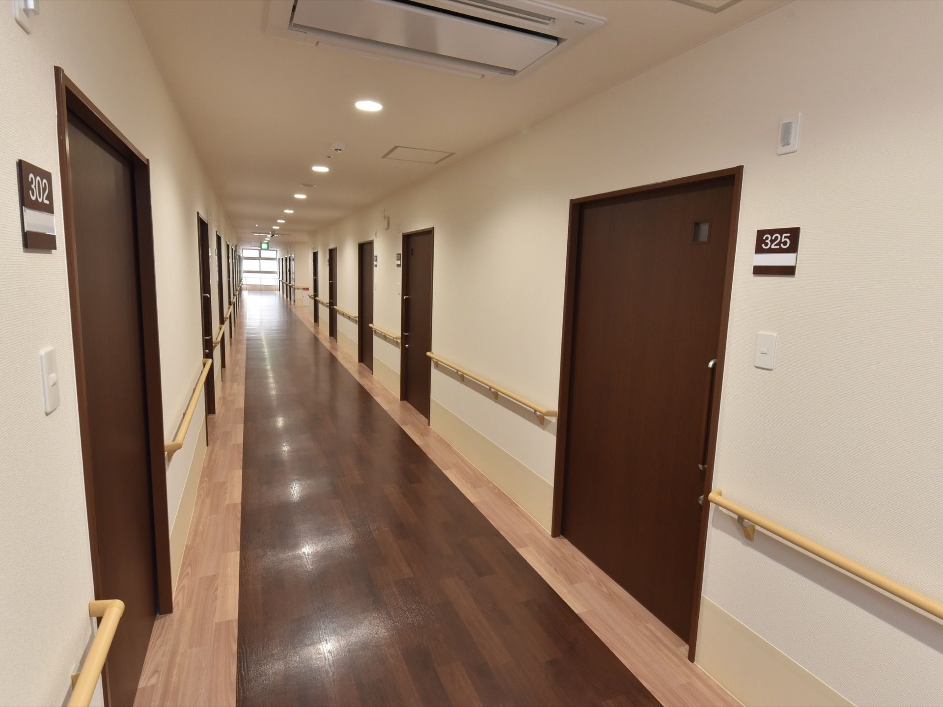 まっすぐ伸びる廊下の左右に、焦げ茶色の居室ドアが並んでいる。部屋番号プレートの下にはインターホンが付いている。