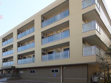 1階部分はこげ茶、2階から4階はベージュの建物で、バルコニーの目隠しはアクリル板