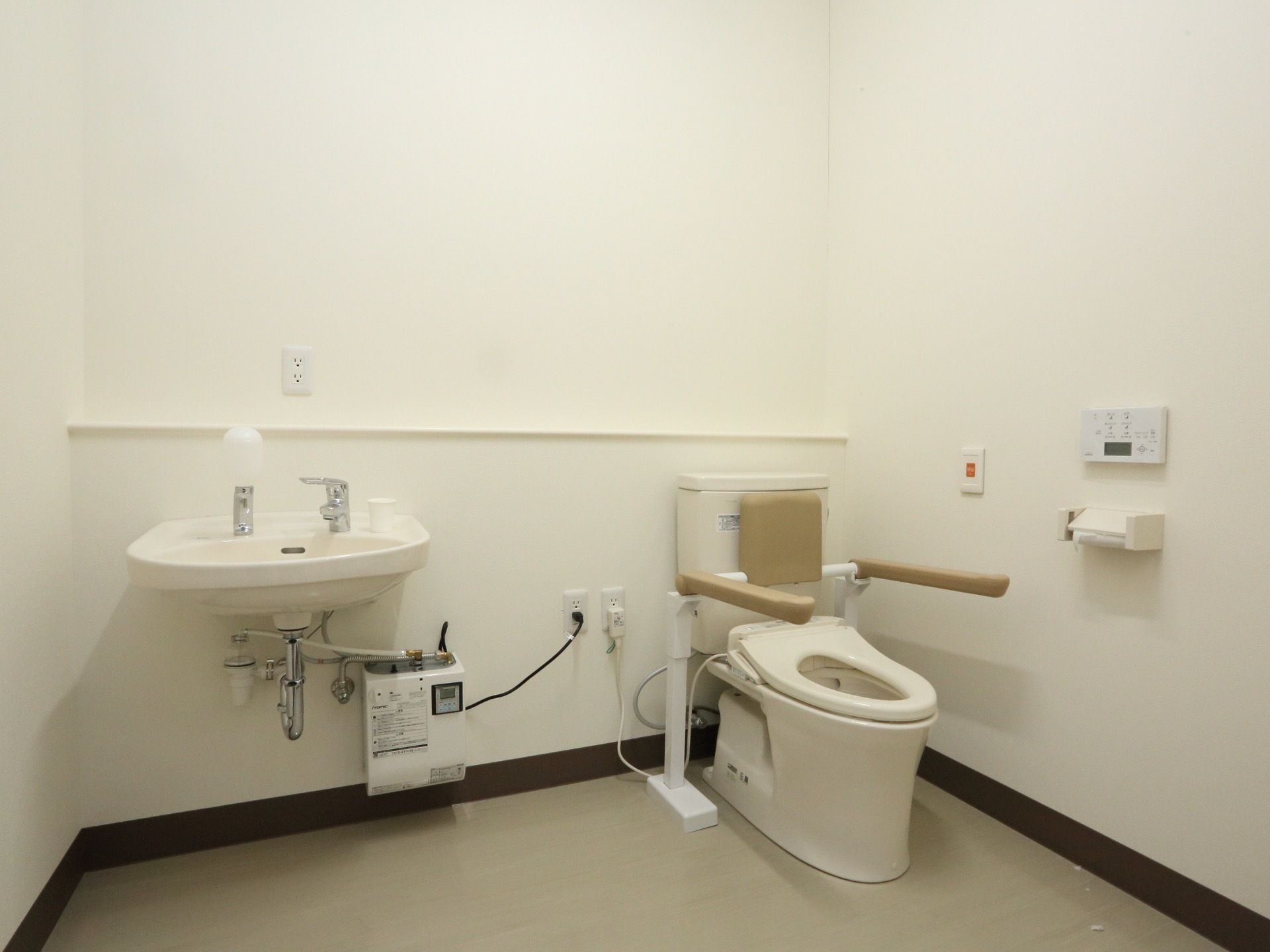 温水洗浄便座のトイレを設置しており、操作ボタンが壁にあるので押しやすい。便器には背もたれとひじ掛けがあり、立ち上がる際に便利である。