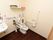 収納棚が多く設置された個室トイレで、洗剤やトイレットペーパなどが置かれている。壁にはナースコールが設置されている。