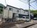 ２階建ての施設は、周りに山々の緑が広がっており、道路に面している。施設の玄関前には、駐車場が確保されている。