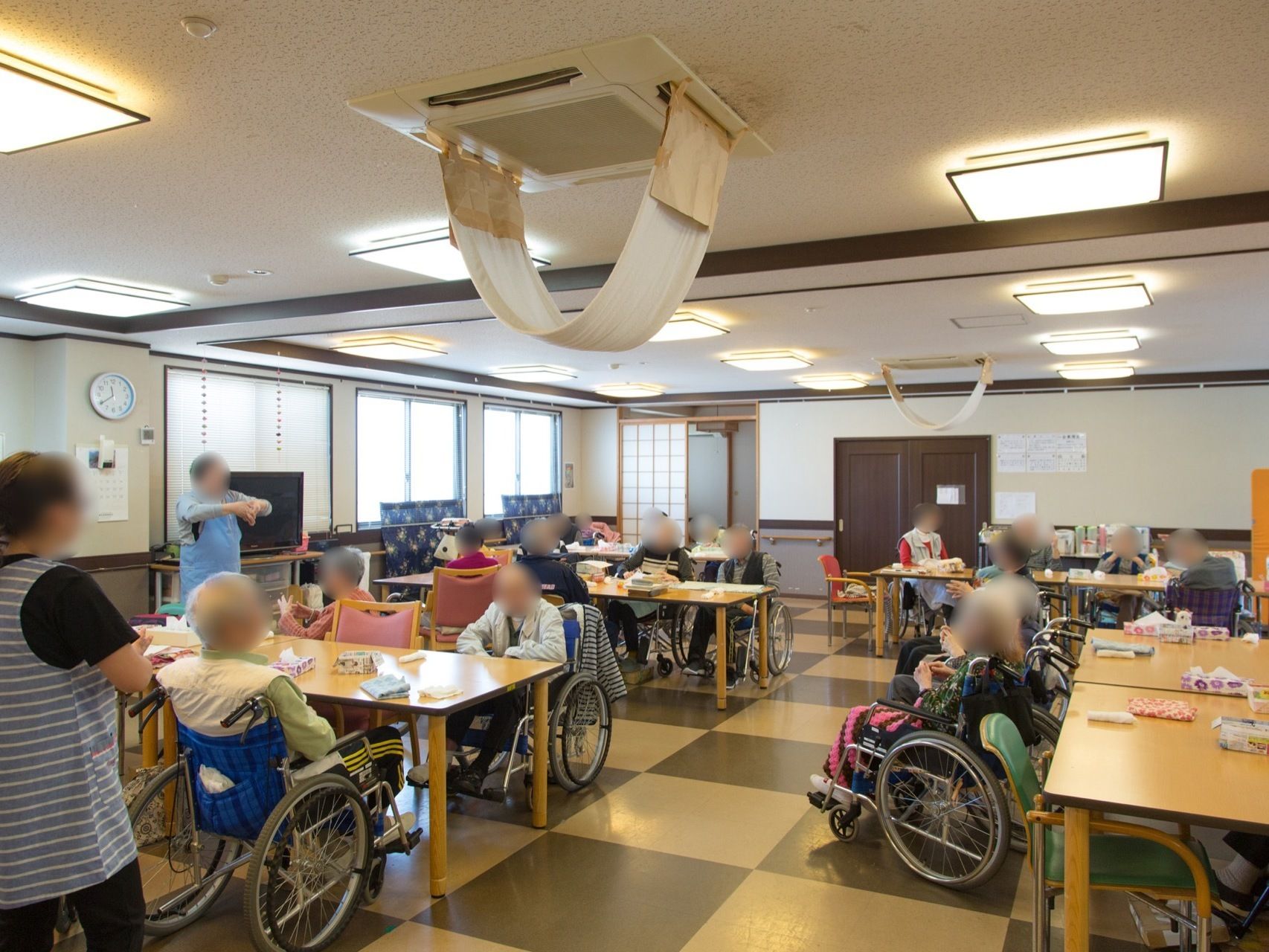 入居者様がスタッフの指導のもとレクリエーション活動をしている。窓がたくさんあり、天井には照明が多く取り付けられている。