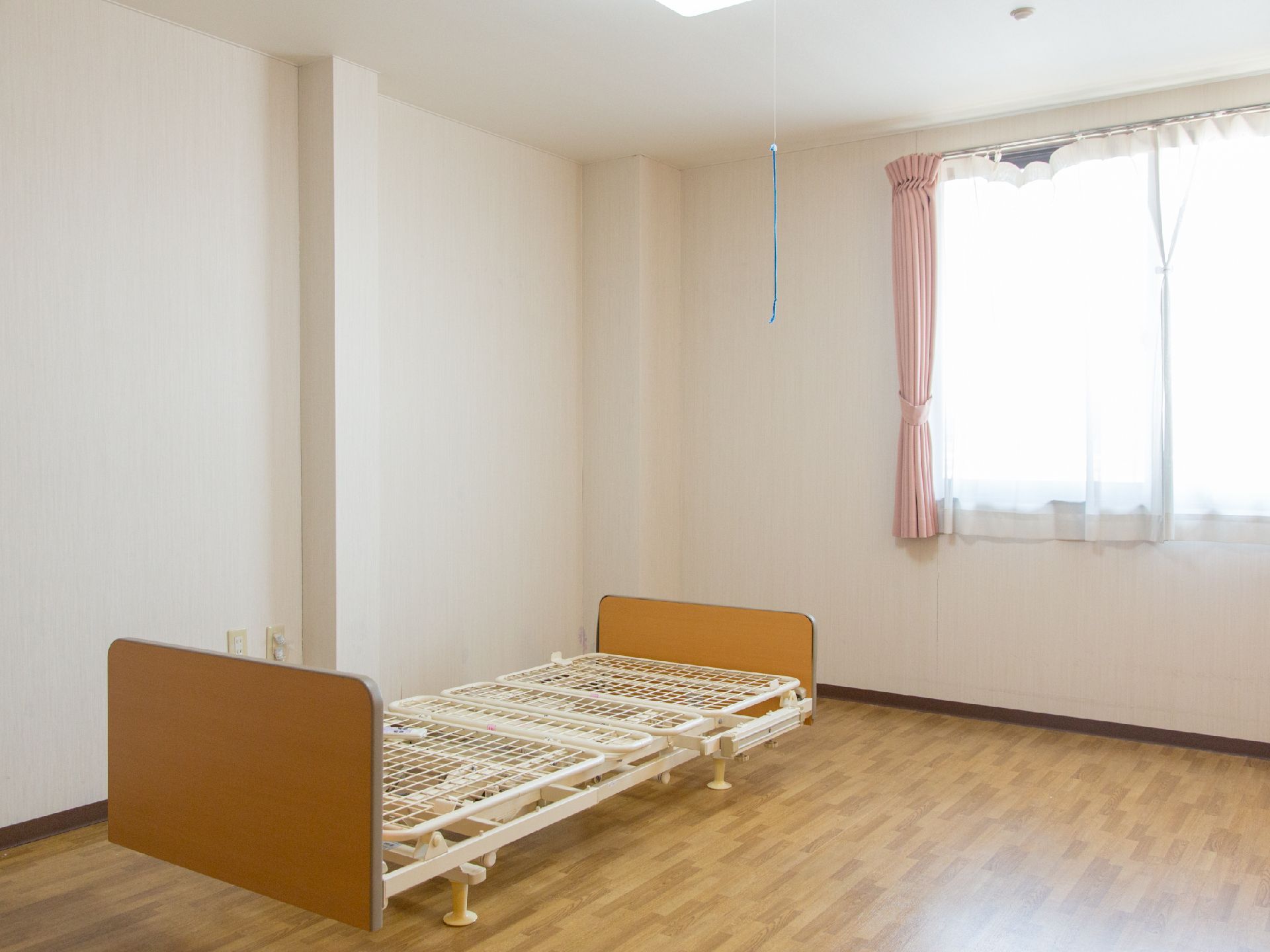 窓から陽の光が差し込み、利用前のマットレスがないベッドが置かれた広い居室