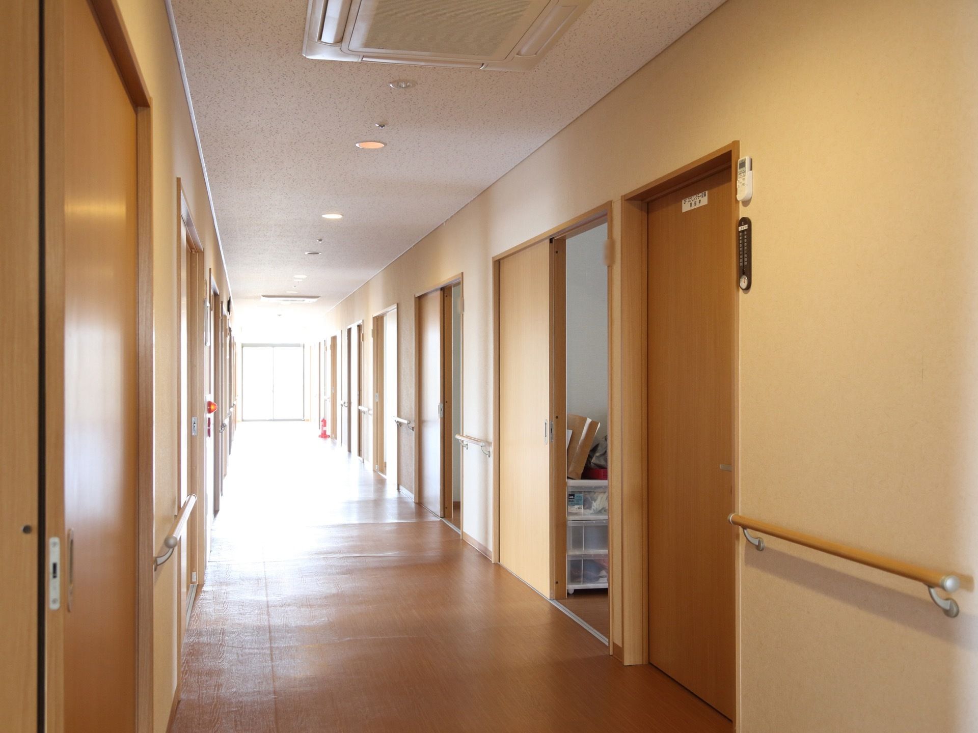廊下は奥行きがあり、両サイドには入居者様用の居室が並んでいる。居室の扉は、ベージュ色の引戸が取りつけられている。