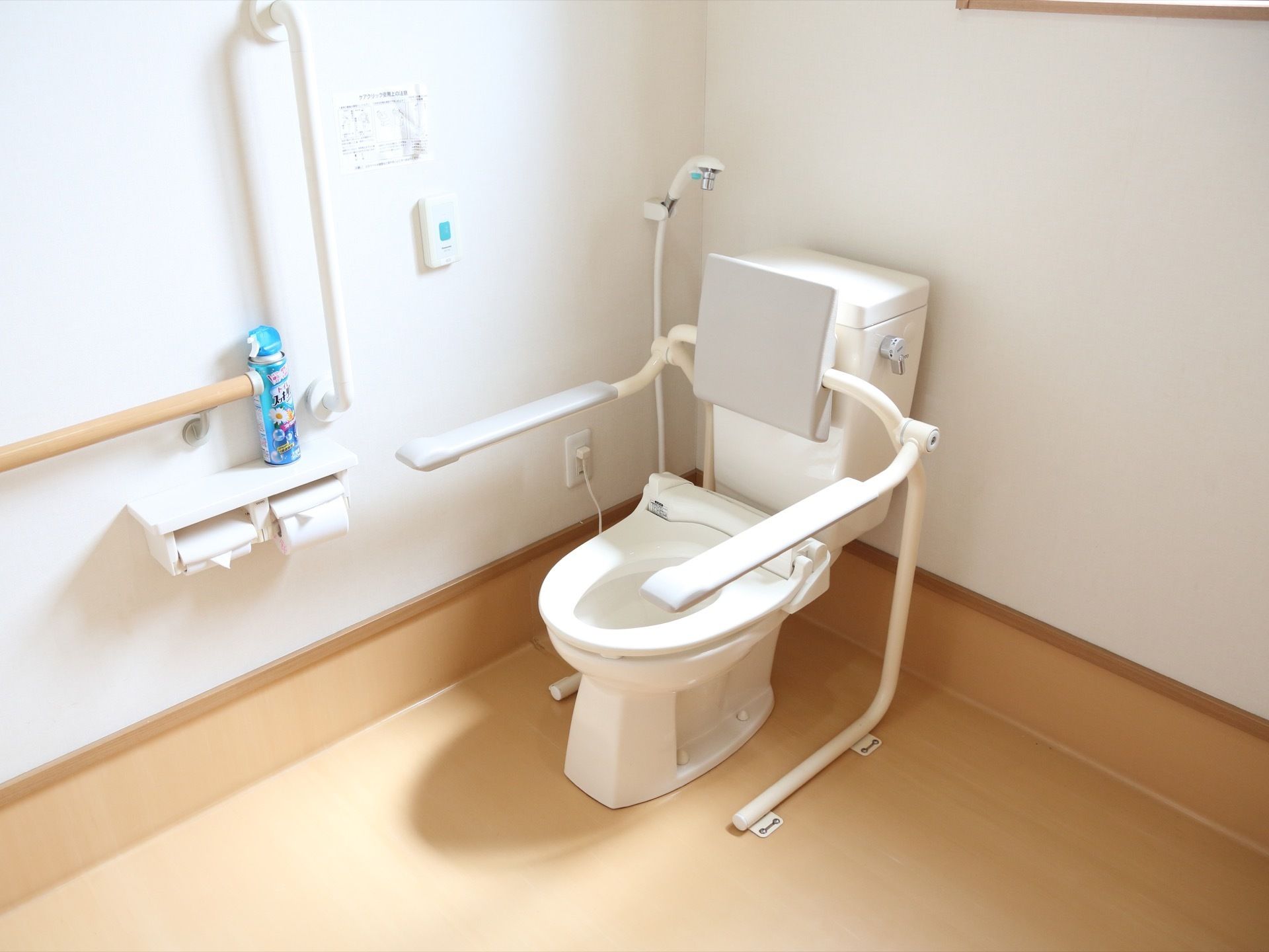 トイレには、トイレットペーパー掛けや手すり、ひじ置きなどが取りつけられている。壁には、緑色の呼出ボタンが設置されている。