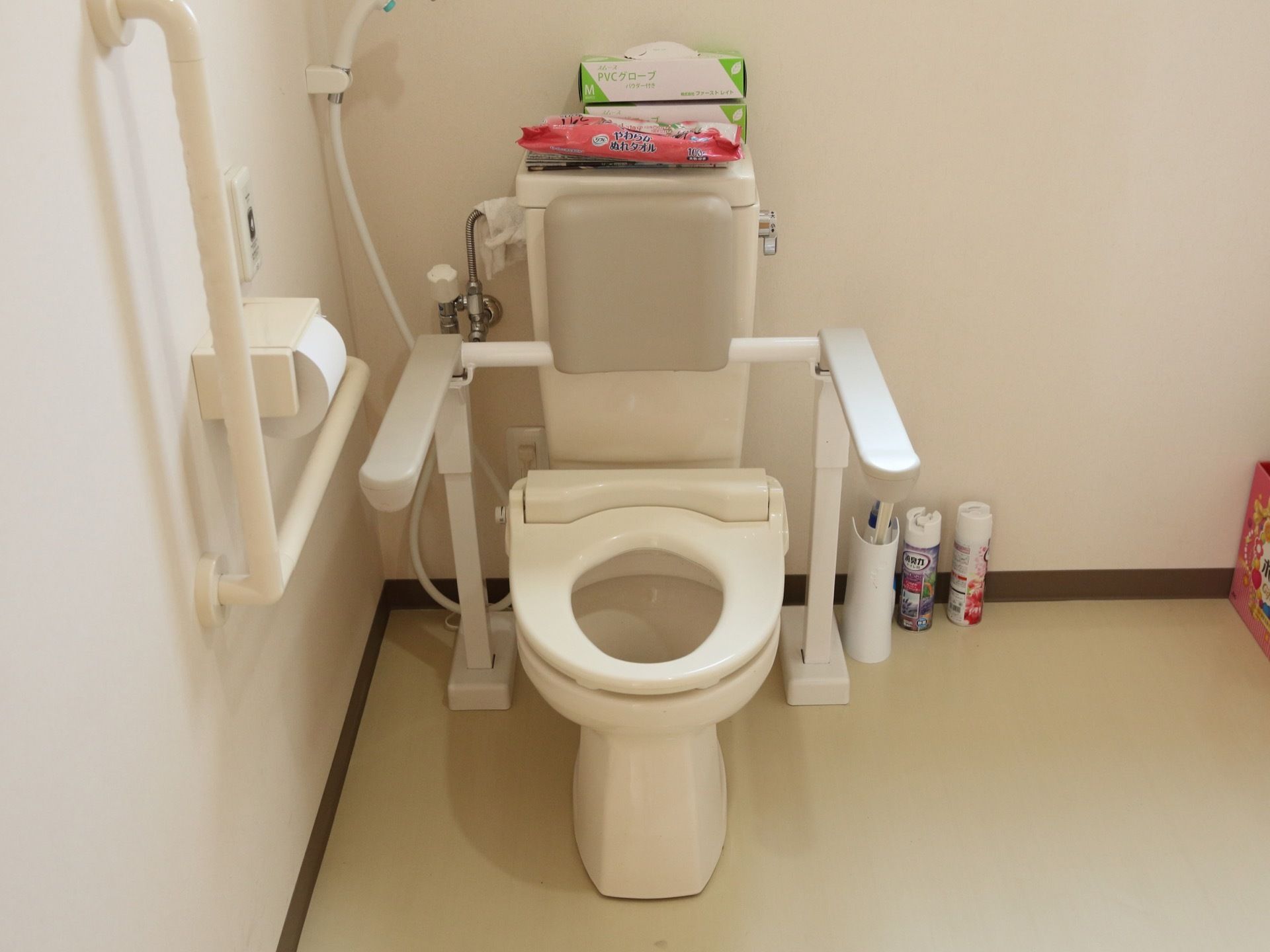 便座の横にはね上げ式のひじ掛けが設置されている。シャワーが設置されている。壁には手すりが設置されている。