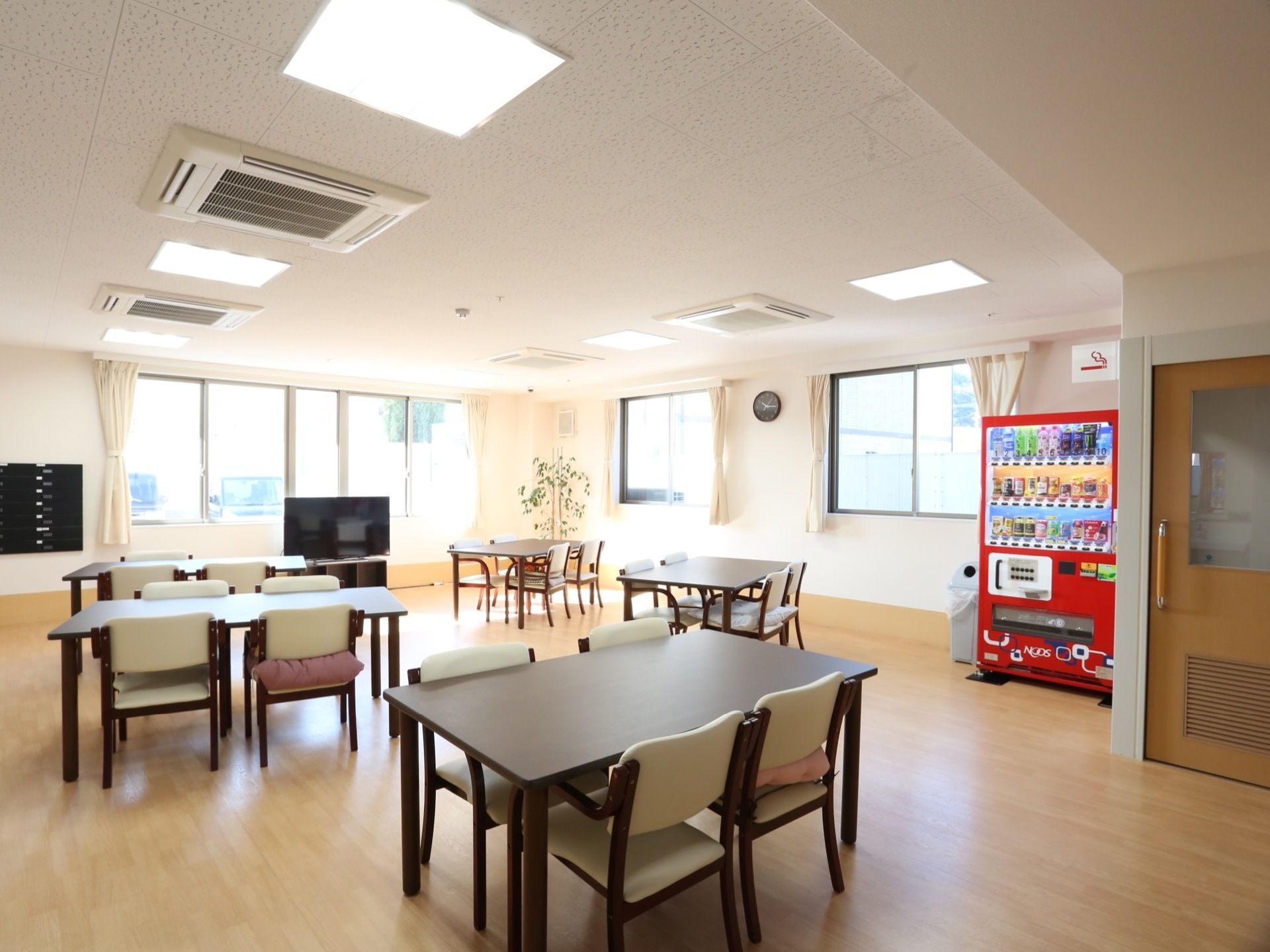 日当たりが良く、開放的な空間にダイニングテーブルがいくつも並んでいる。自動販売機が設置されており、窓側にテレビが用意されている。