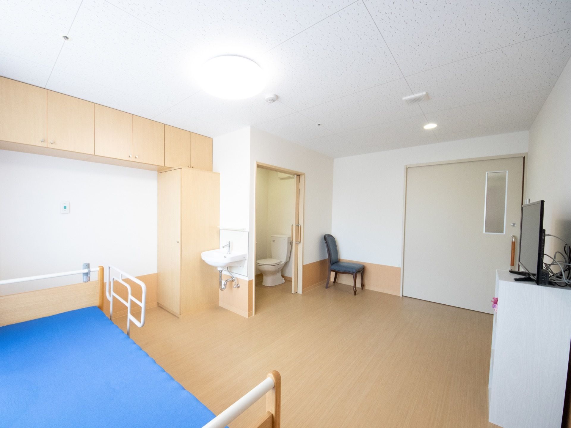 ベッド、クローゼット、チェア、テレビなど広い部屋に必要な家具が一式取り揃えられている。トイレや洗面台も室内に設置されている。